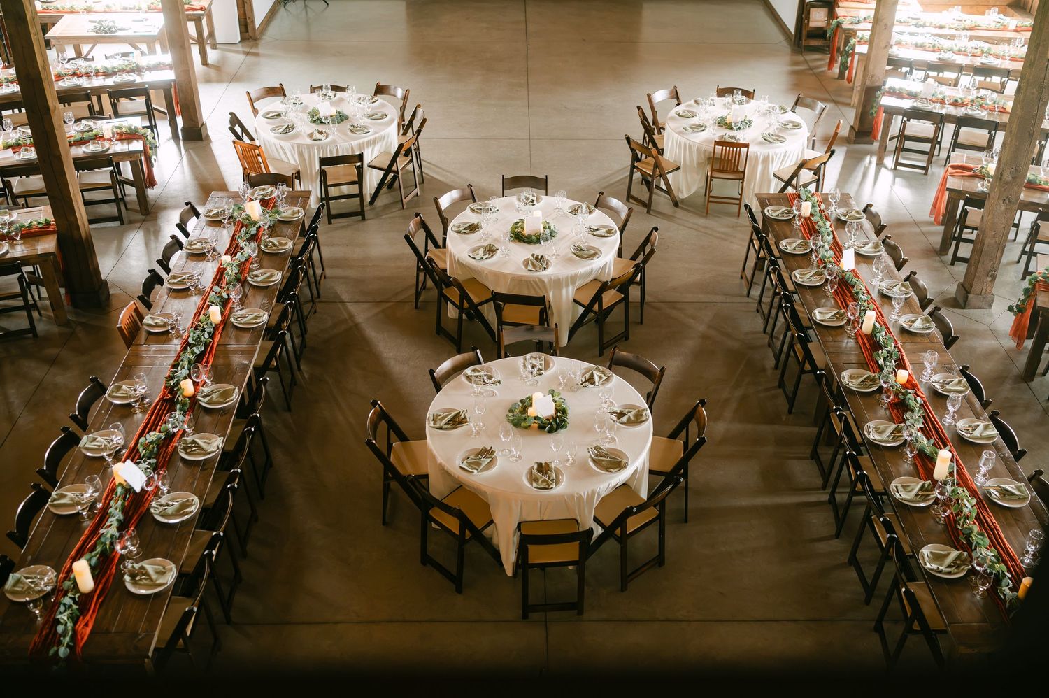 Elegant wedding reception hall with round and long rectangular tables set with white linens and red floral centerpieces.