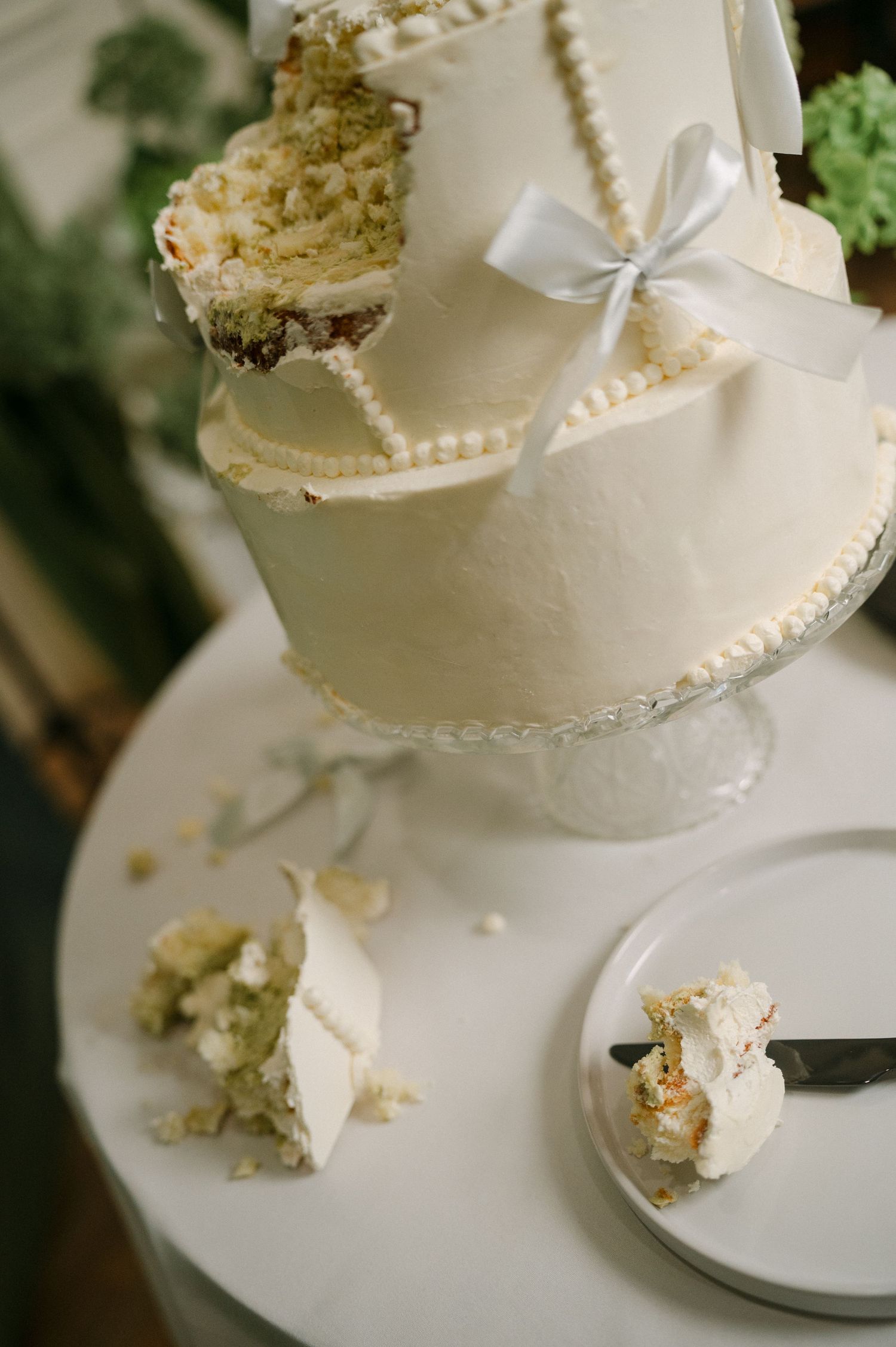 Partially cut two-tier white wedding cake with pearl trim and a blue ribbon bow.