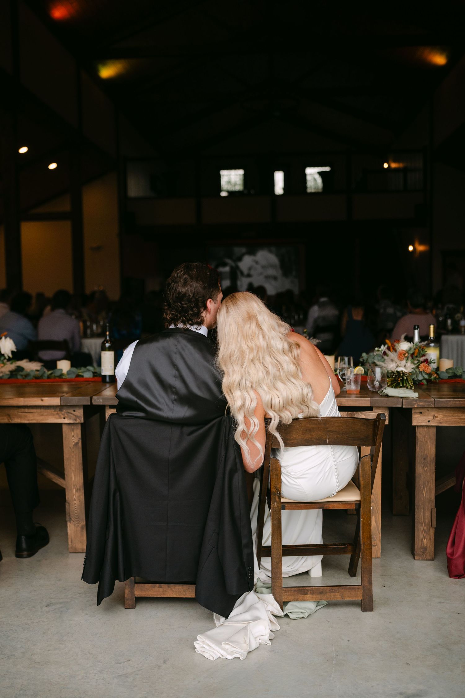 Bride and groom share a kiss at their sweetheart table during wedding reception in a rustic barn venue.