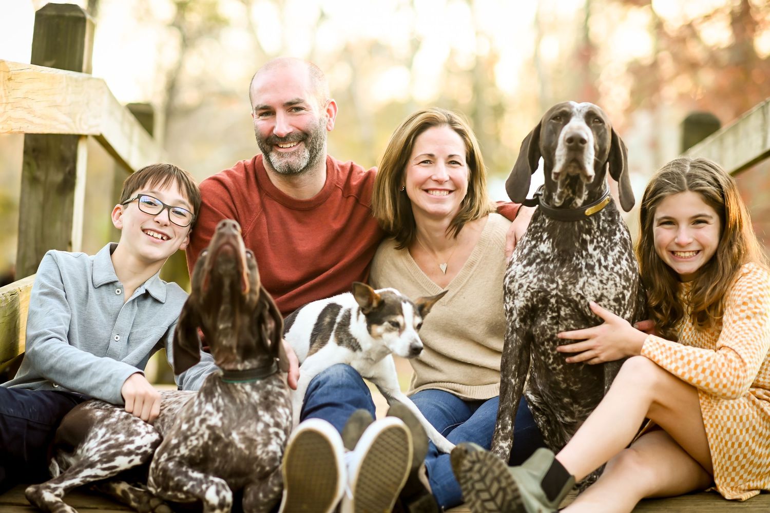 Family of four smiling with two German Shorthaired Pointers and a small dog on outdoor steps.