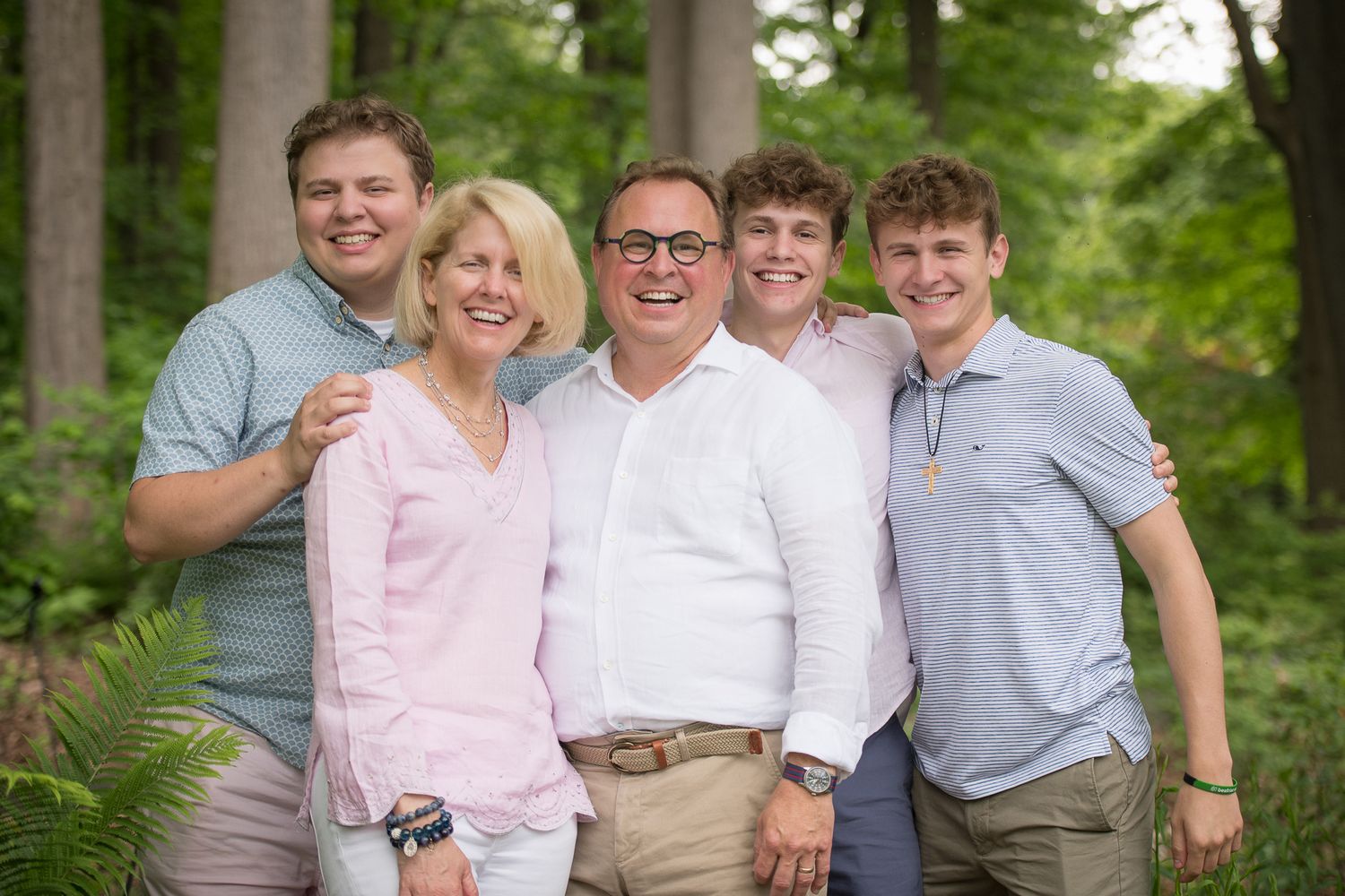 Happy family of five smiling together outdoors in a lush green forest setting for a portrait photo.