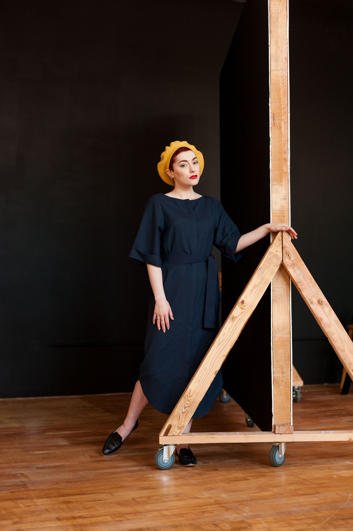 Well dressed woman in a yellow beret posing beside a studio backdrop