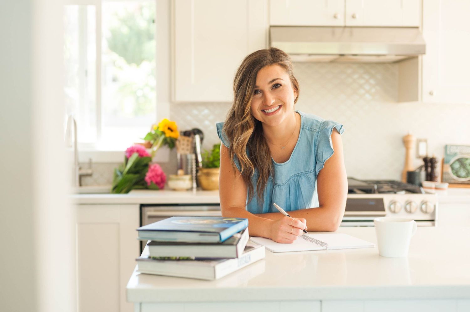 Young woman leans on a kitchen counter with a stack of cookbooks in the foreground