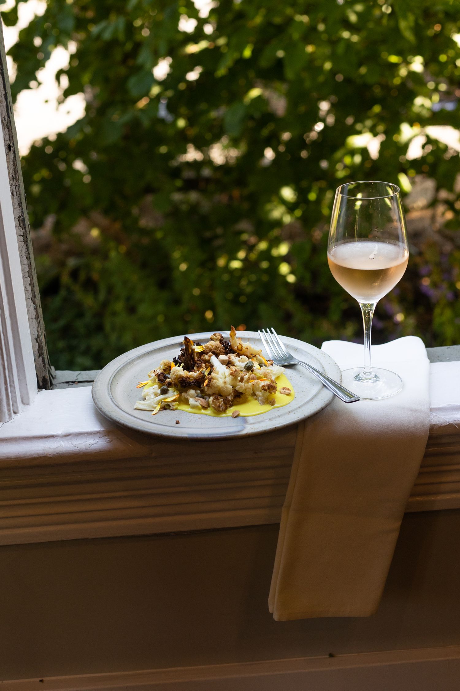 A cauliflower salad and glass of white wine on a window sill