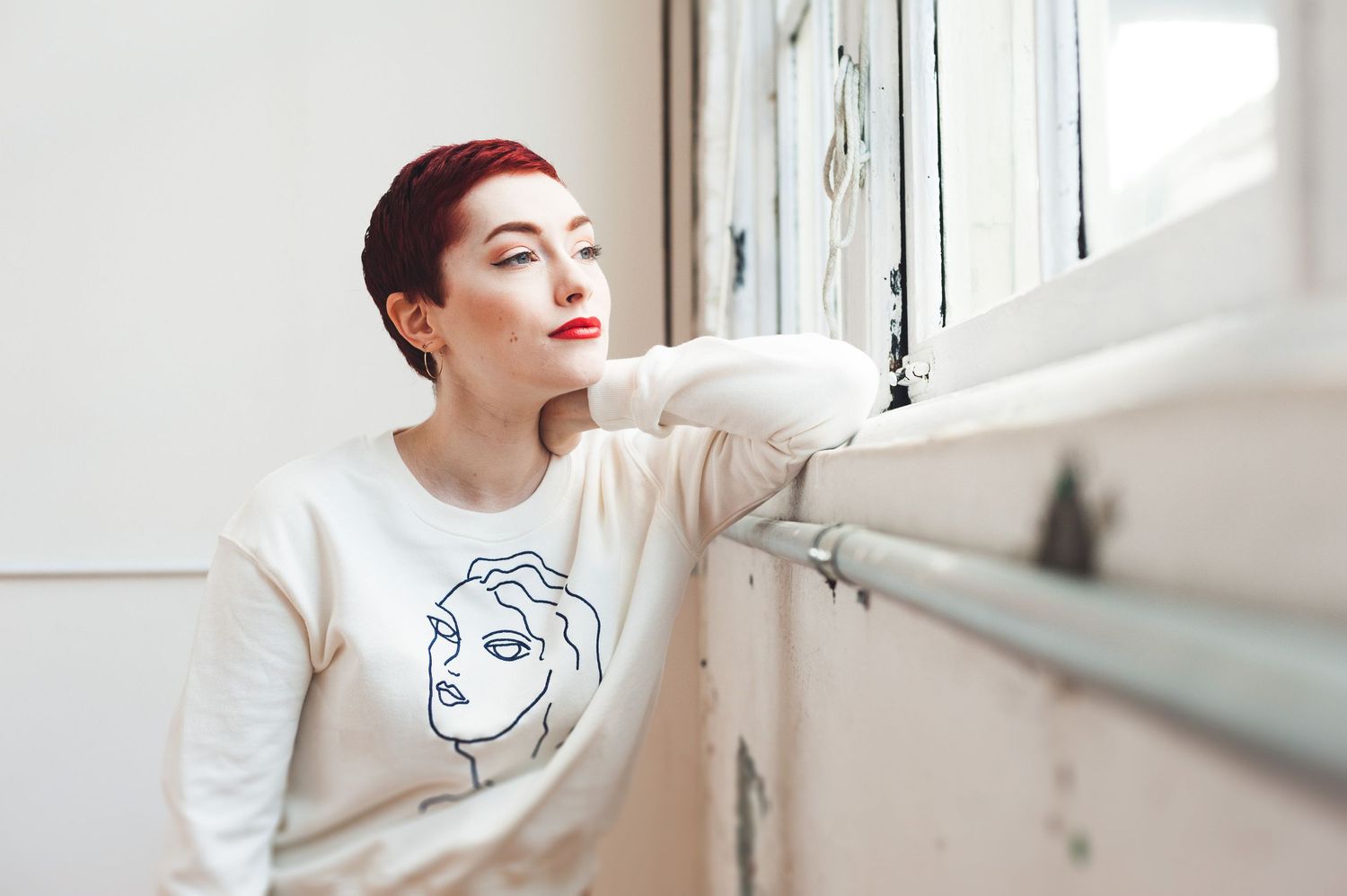 Woman with short red hair looking out a window