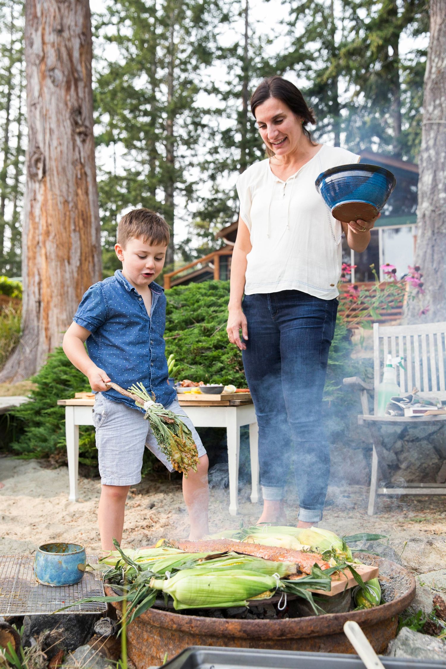 woman and boy attending to a fire pit with corn
