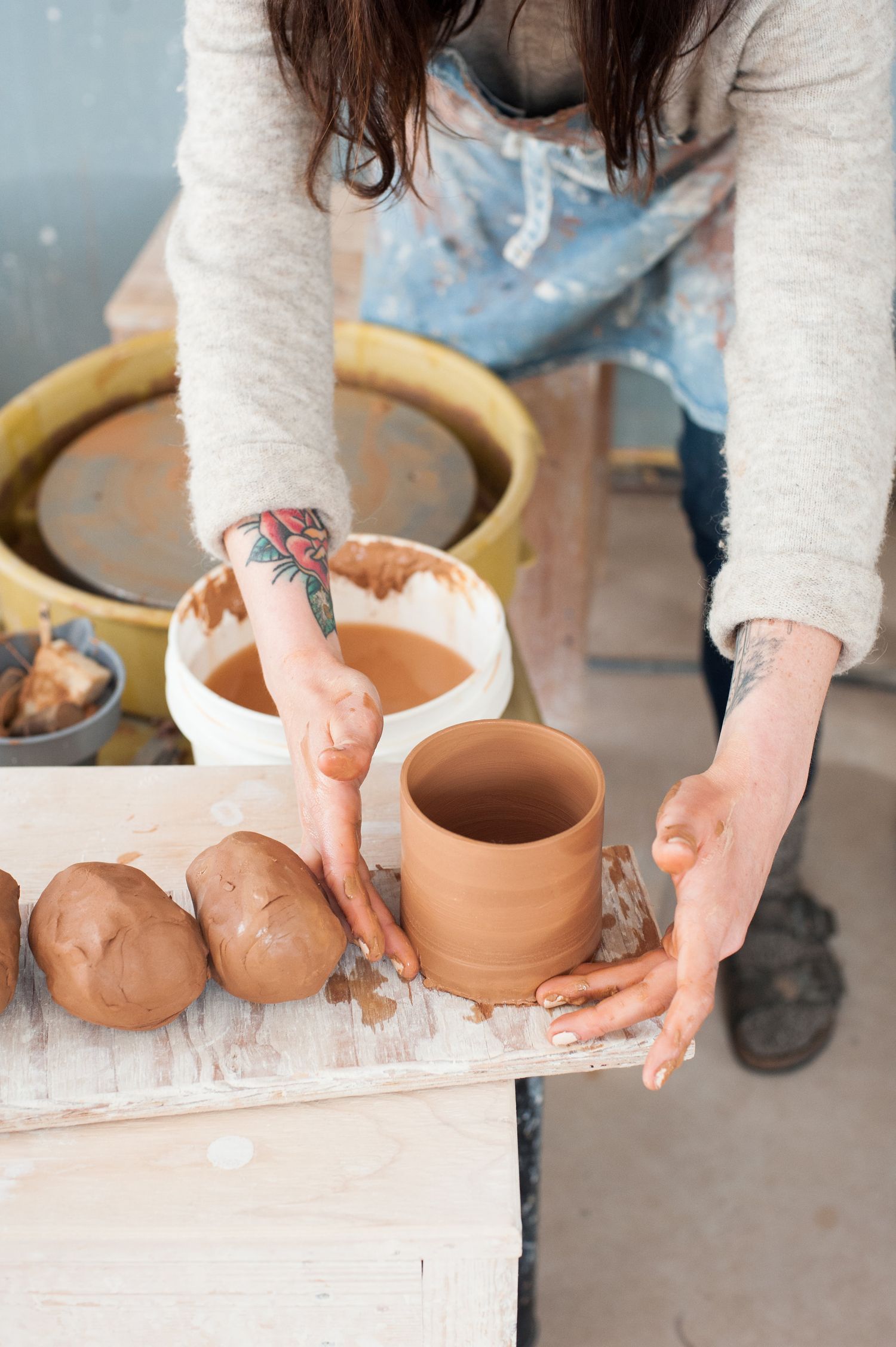 Woman holding a clay pot that she has just made on a pottery wheel