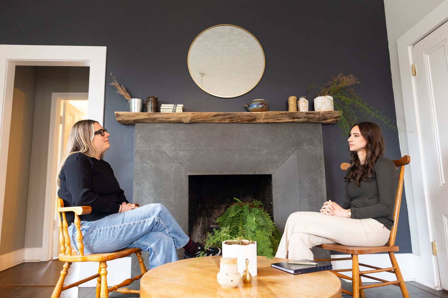 two women have a conversation in front of a fireplace
