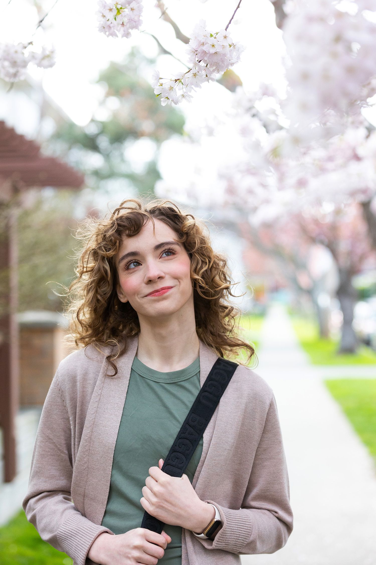 woman with curly hair looking upward toward a canopy of cherry blossoms