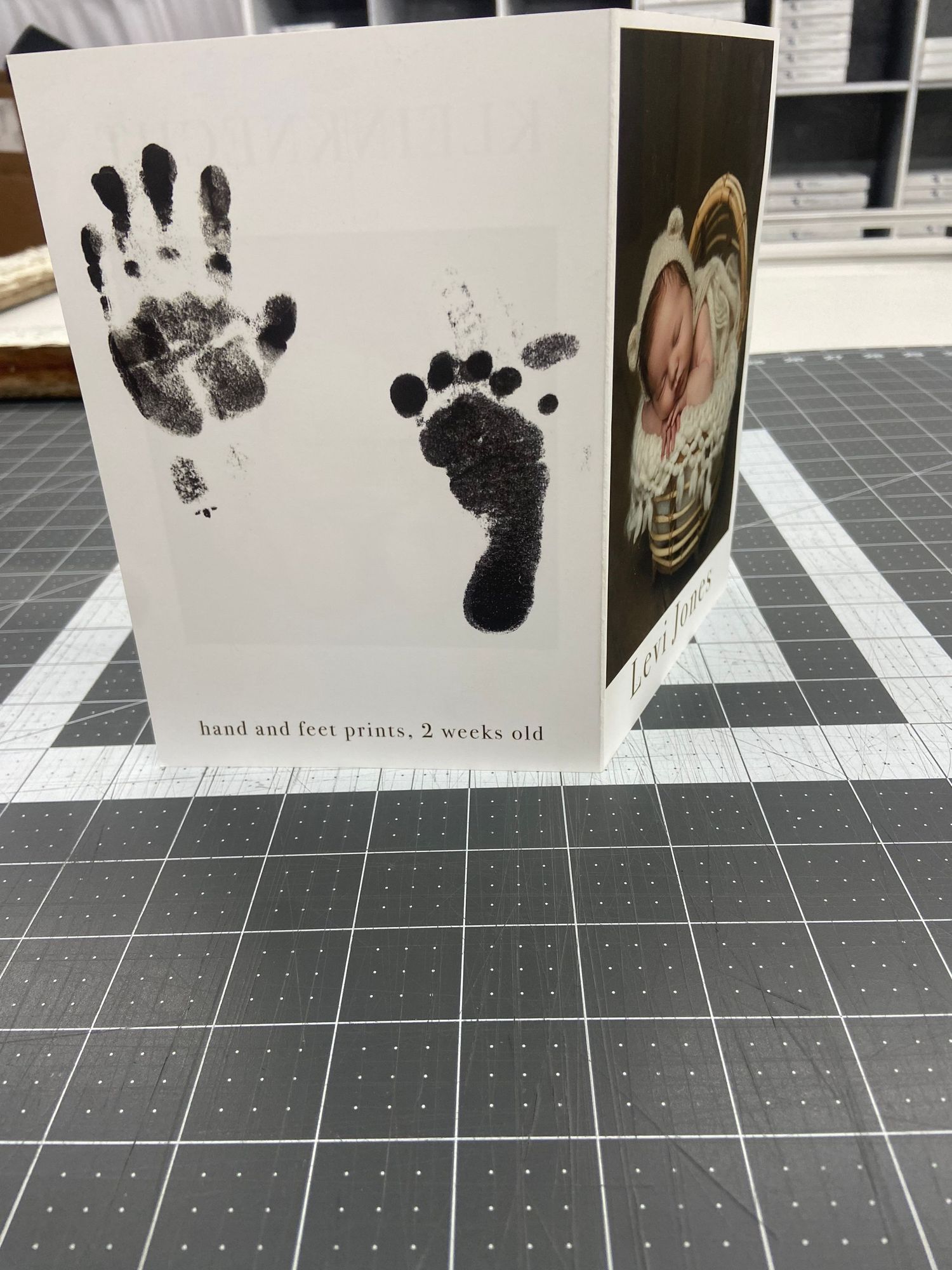 Baby keepsake card featuring black ink handprint and footprint with newborn photo.