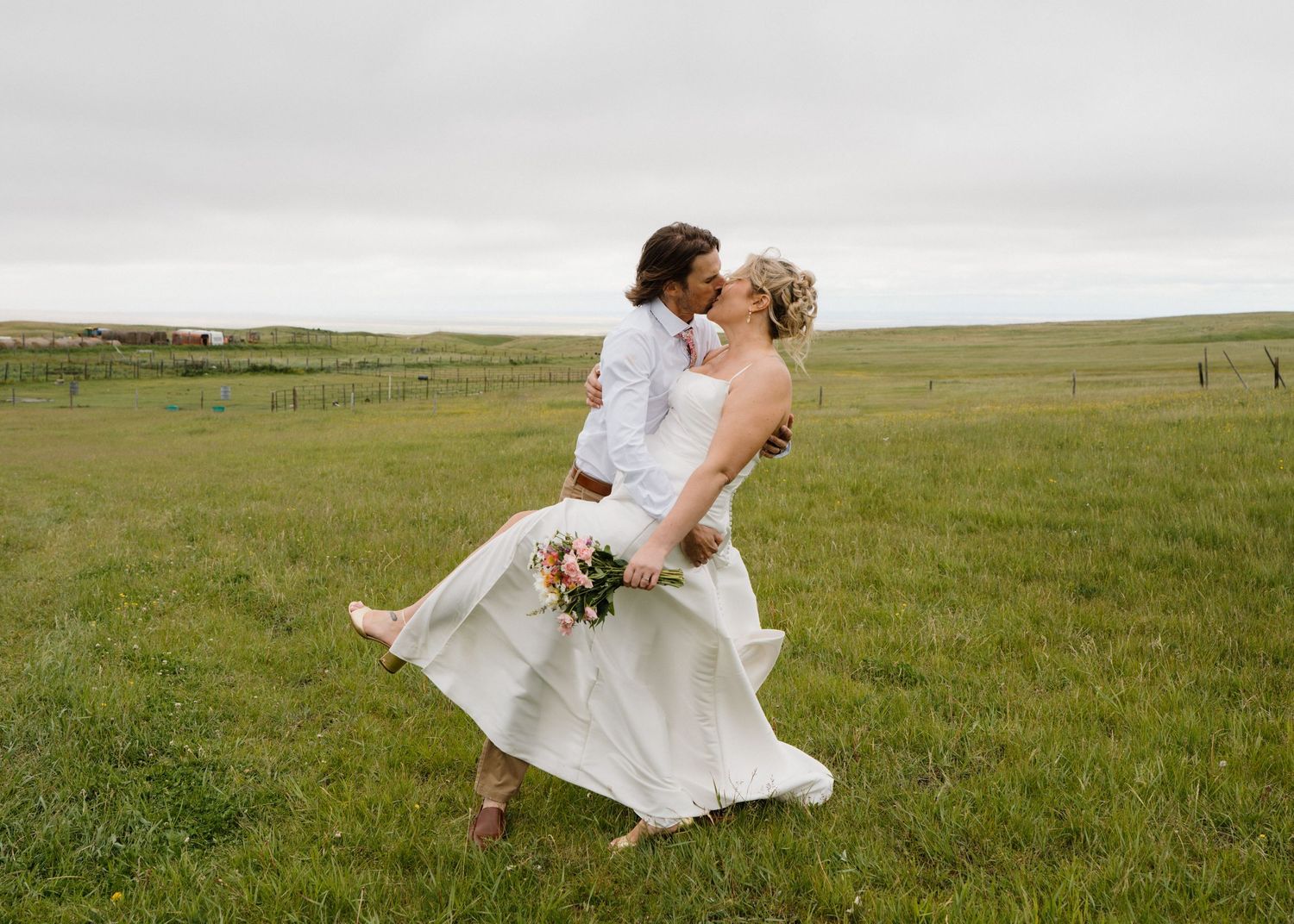Bride and groom sharing a romantic kiss in a lush green field on their wedding day.