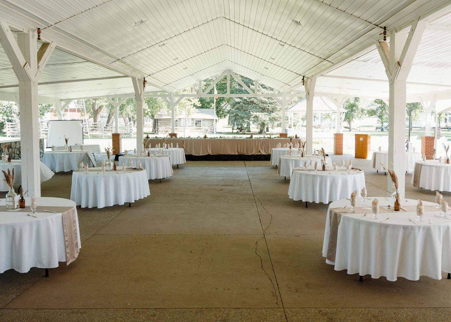 Elegant outdoor wedding reception venue with white round tables under a open-air pavilion with white wooden structure.
