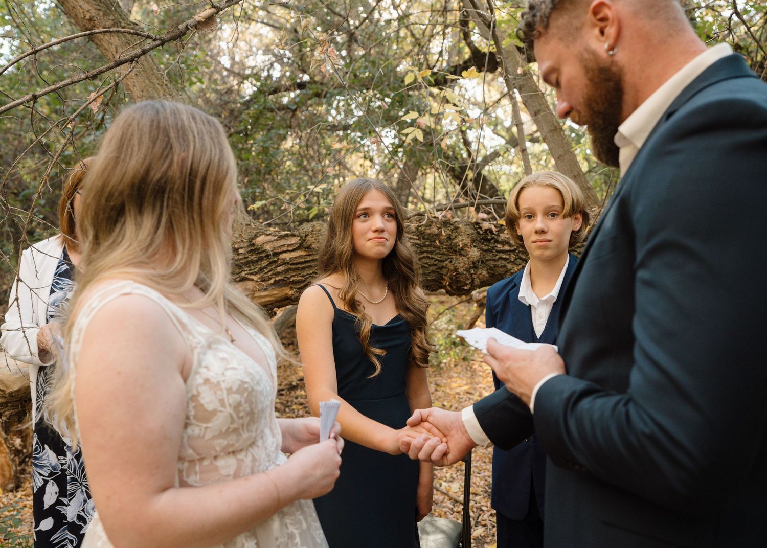 Bride and groom exchanging vows outdoors with two young female witnesses during an intimate woodland ceremony.
