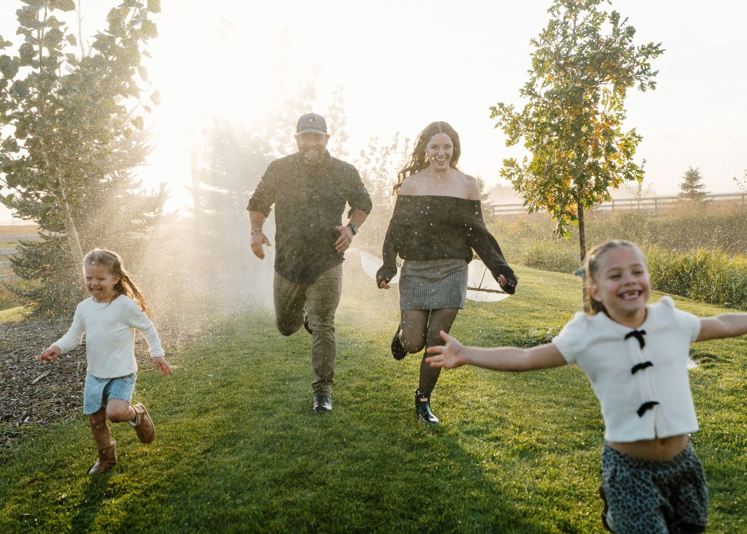 Joyful family with two girls runs through a misty backyard garden in warm golden evening light.