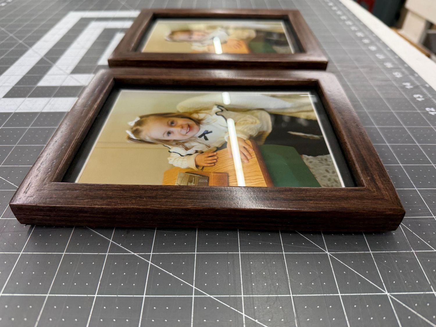 Two matching walnut wood framed photos of a young child displayed on a cutting mat.