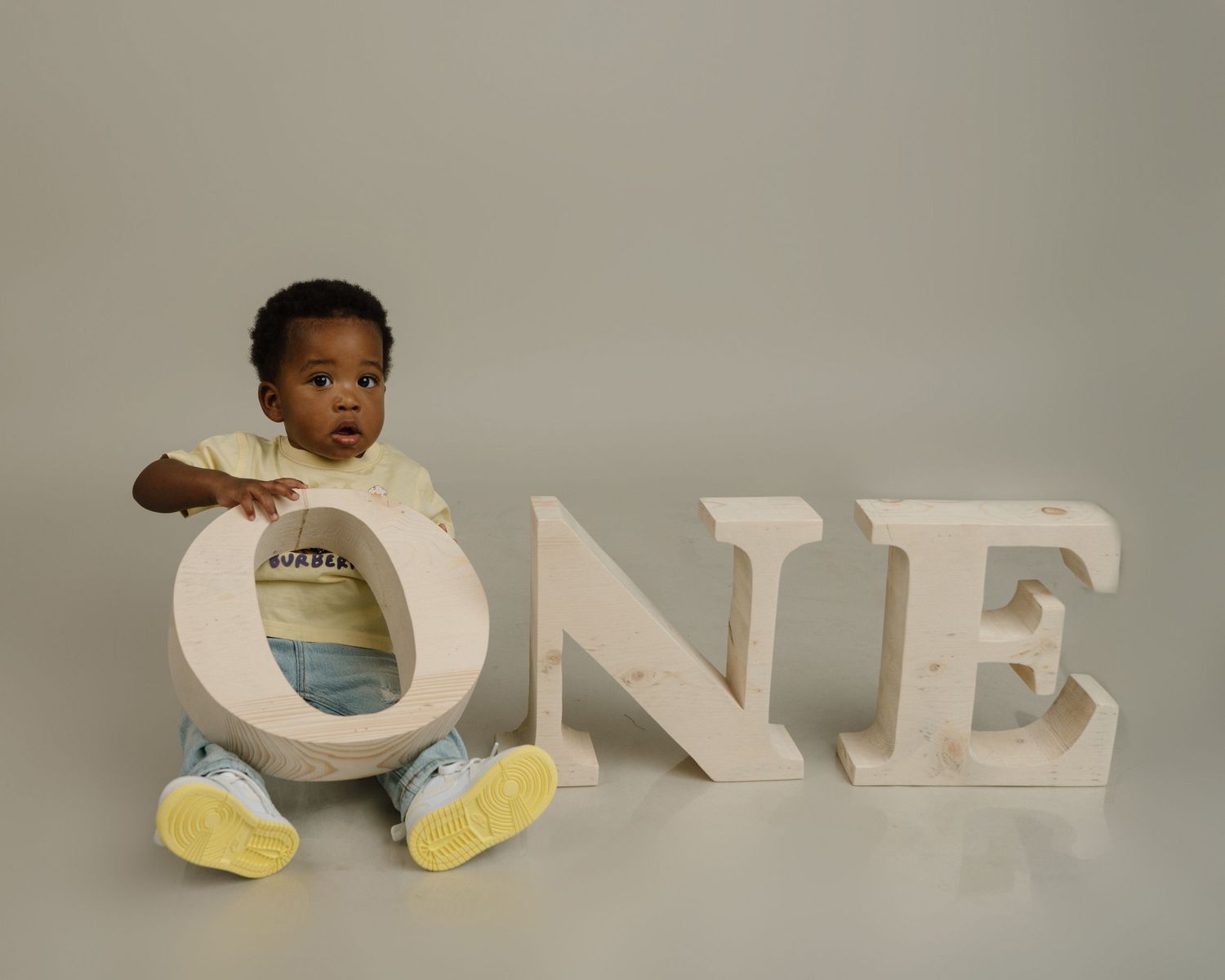One year old baby sitting between large wooden ONE letters for milestone birthday photo.