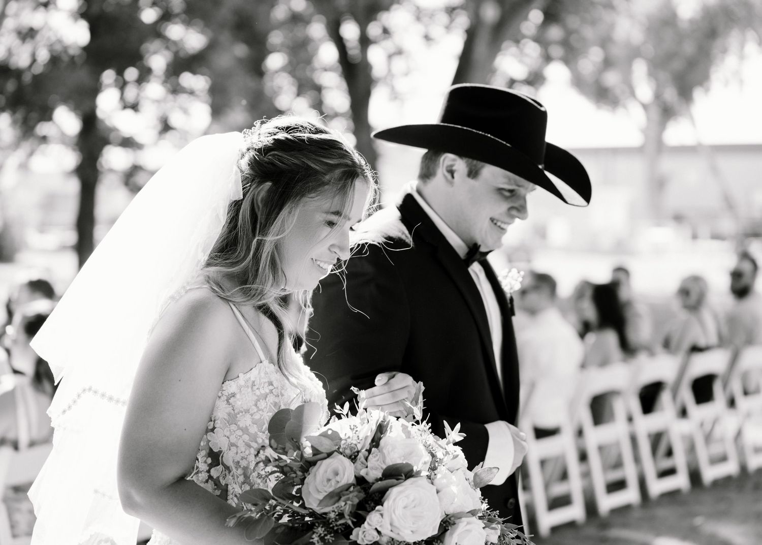 Bride and groom walking down aisle, groom in black cowboy hat, black and white wedding photo.