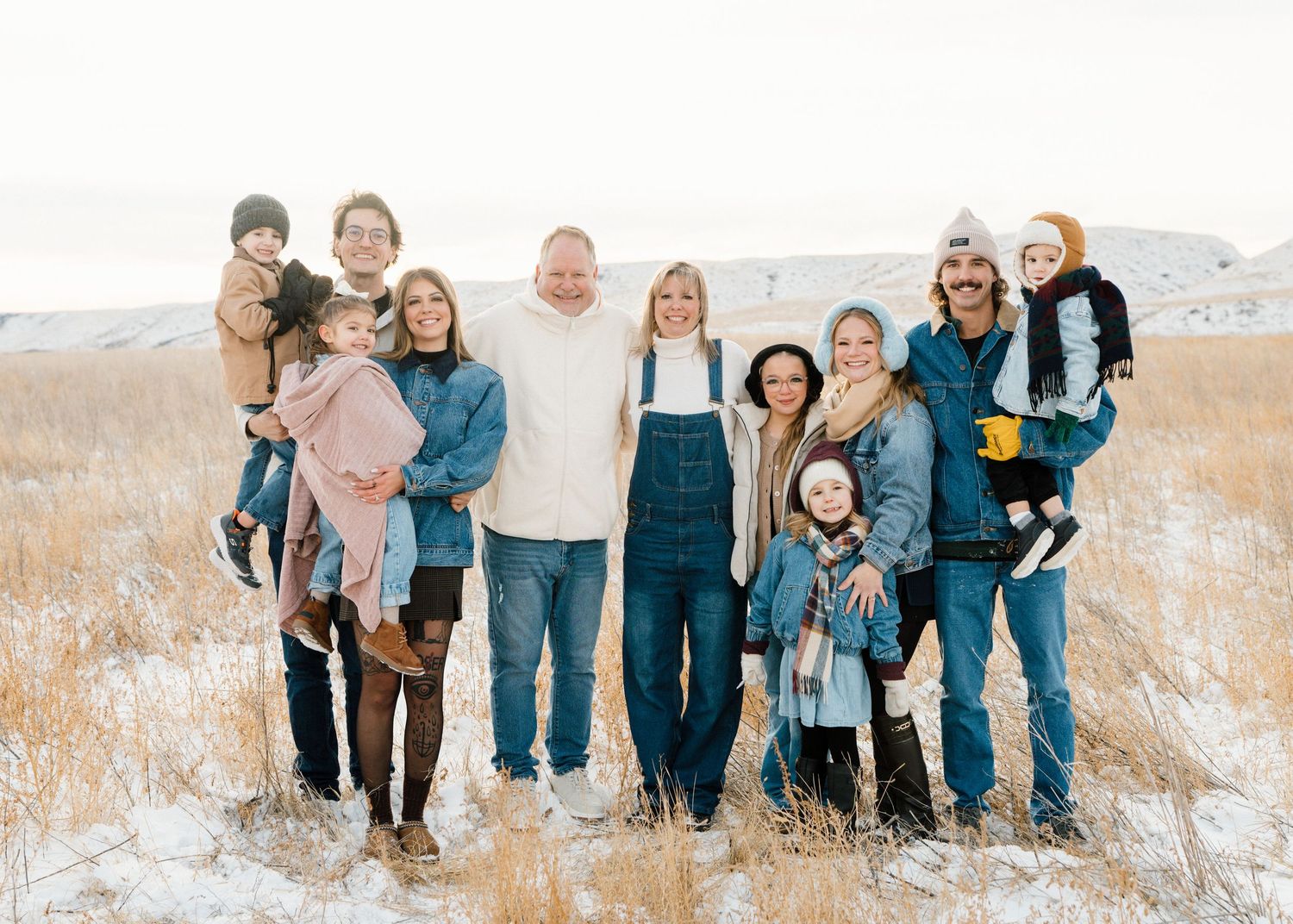 Large family group posing outdoors in snowy winter landscape wearing denim and cozy winter outfits.