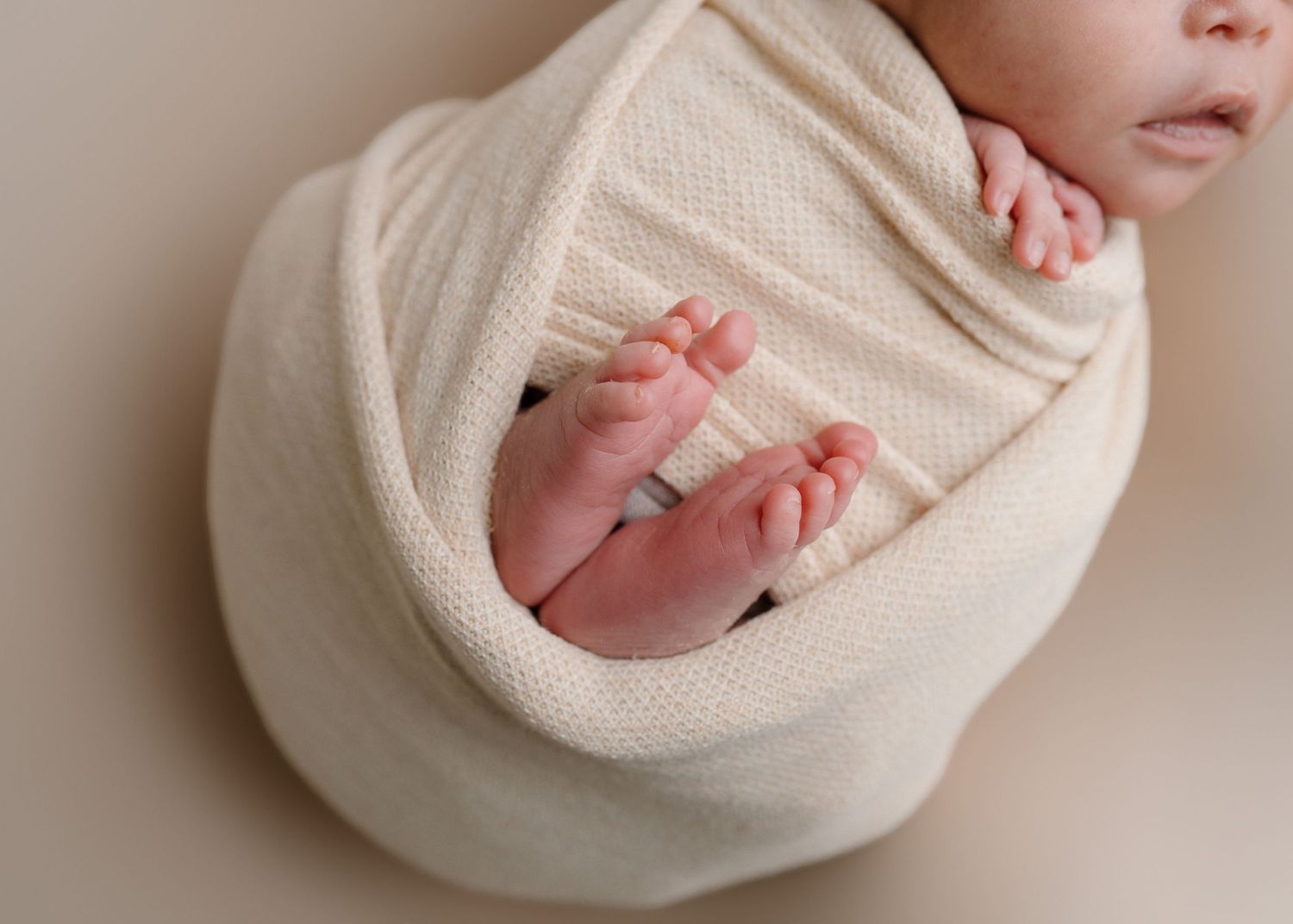 Close-up of newborn baby feet peeking out of cream knit swaddle wrap during newborn photo session.