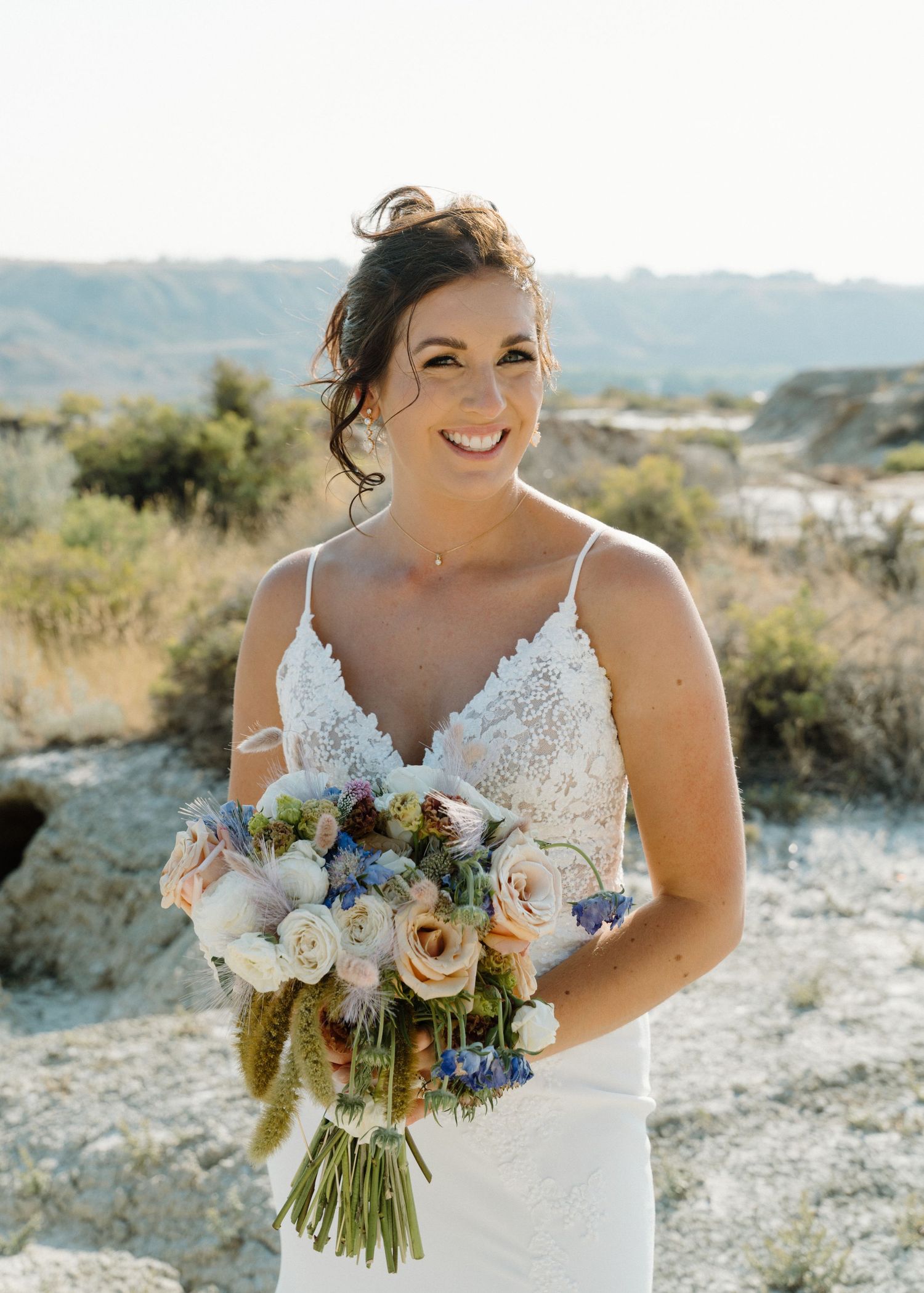 Smiling bride holds colorful bouquet of roses and wildflowers in a sun-drenched desert landscape.