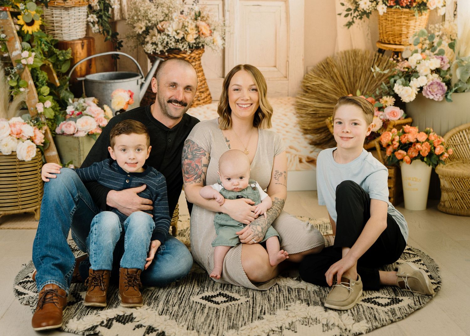Family of five with parents, baby, and two boys sitting together in a floral studio portrait.