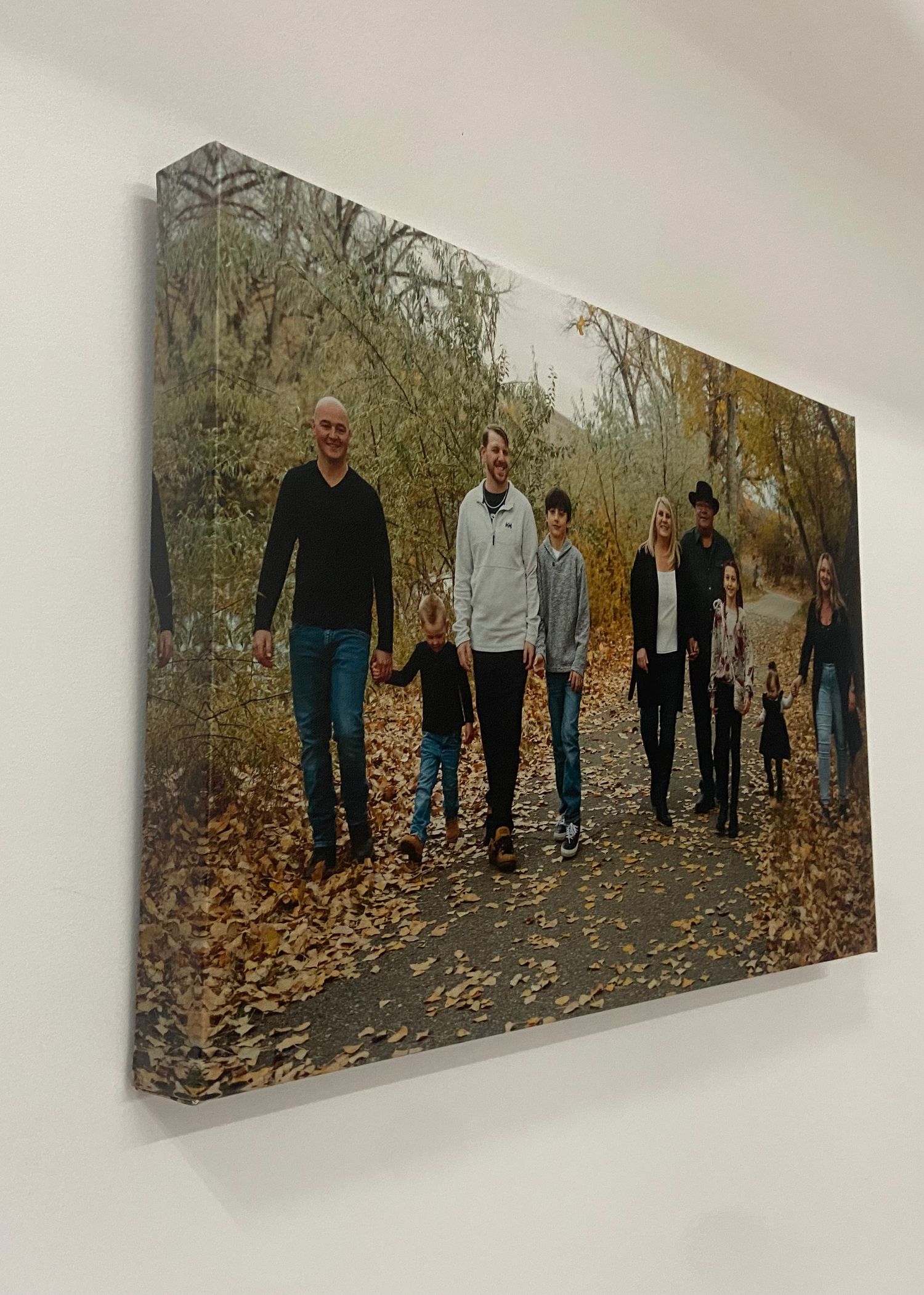 Wide canvas print of a large extended family walking on a leaf-covered path in an autumn forest.