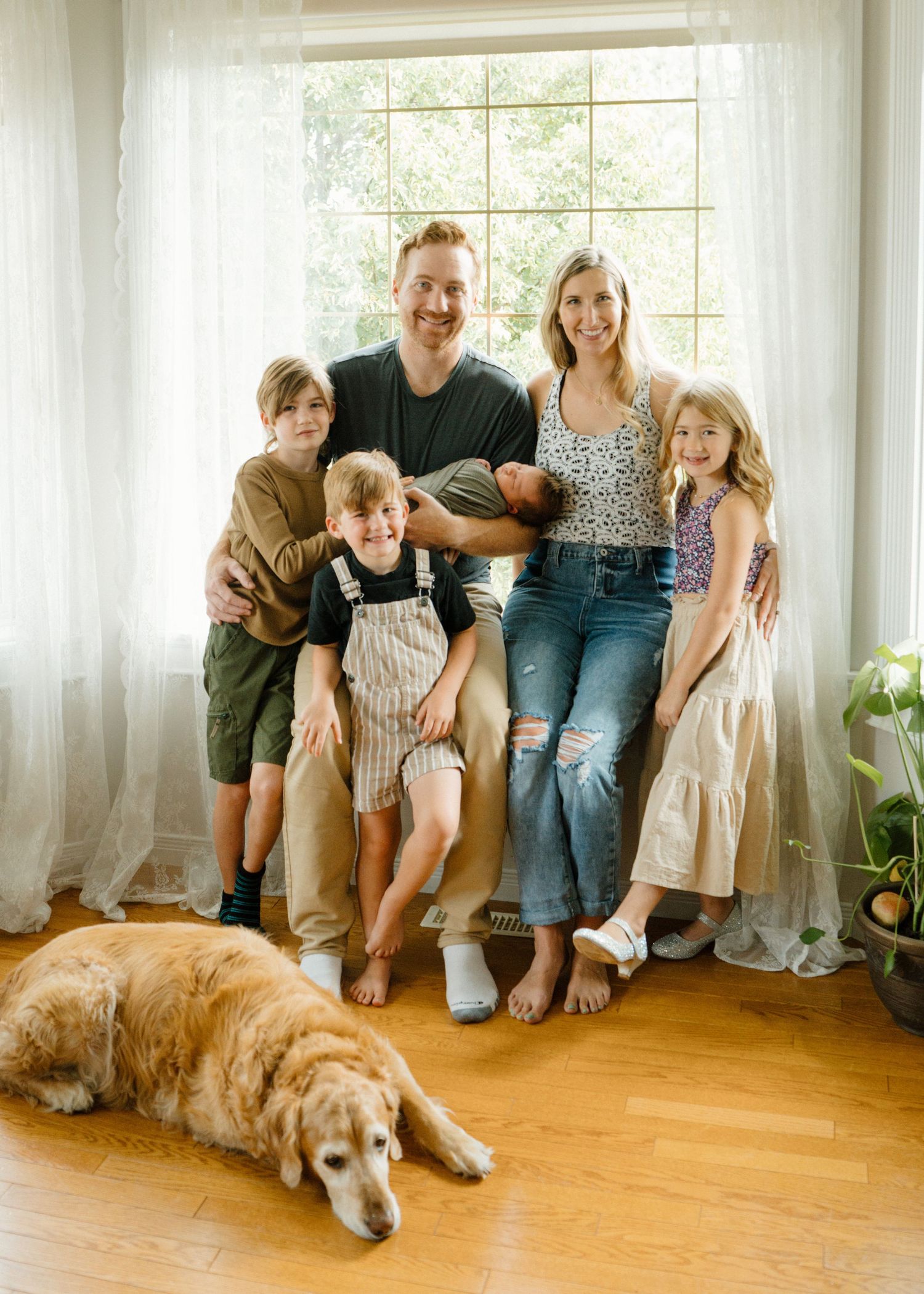 Happy family of five with golden retriever dog posing by bright window indoors.