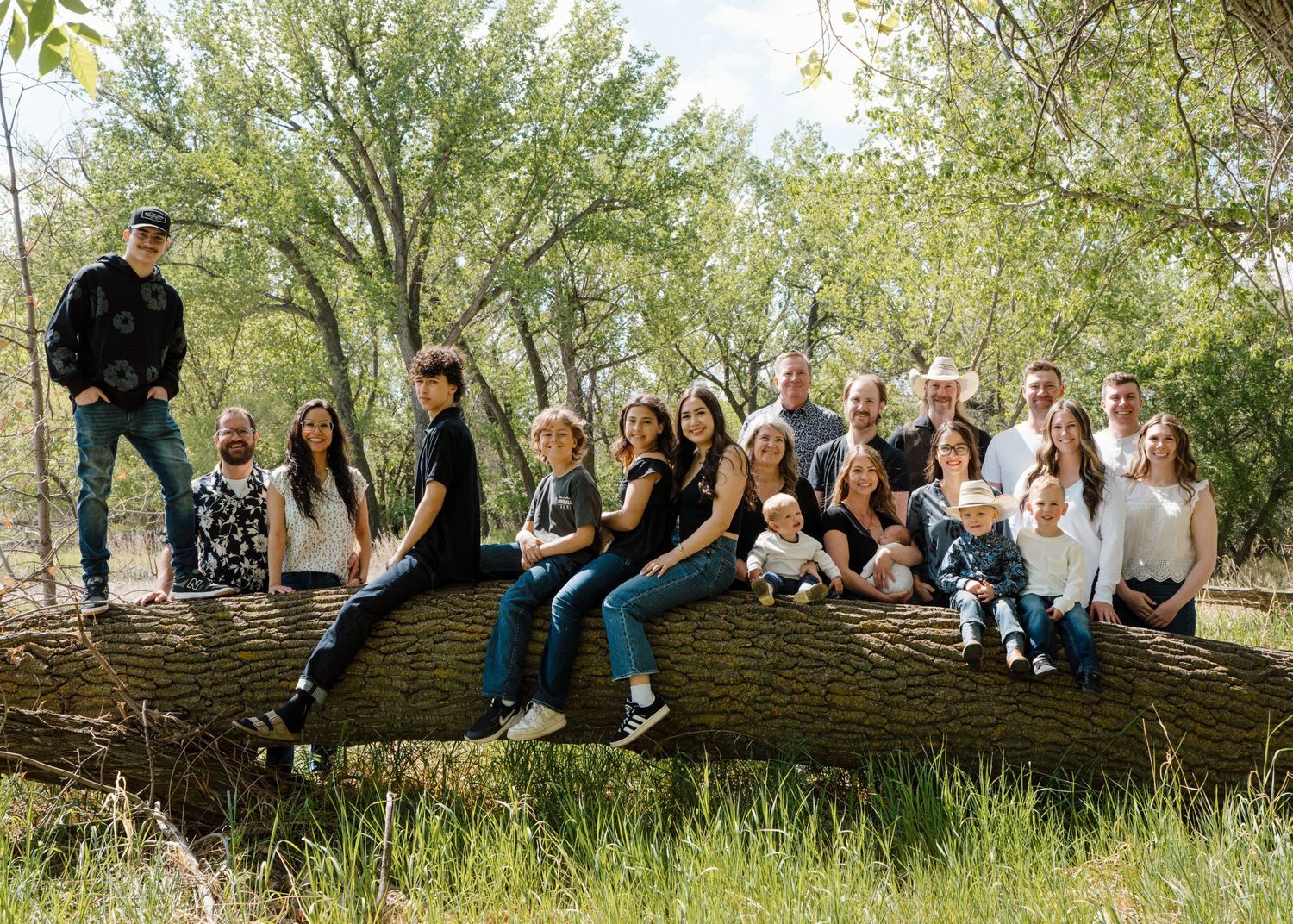Large extended family group portrait sitting on fallen log in lush green forest.