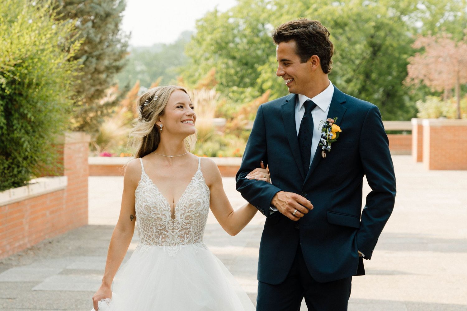 Smiling bride and groom in wedding attire walking together outdoors on sunny day.