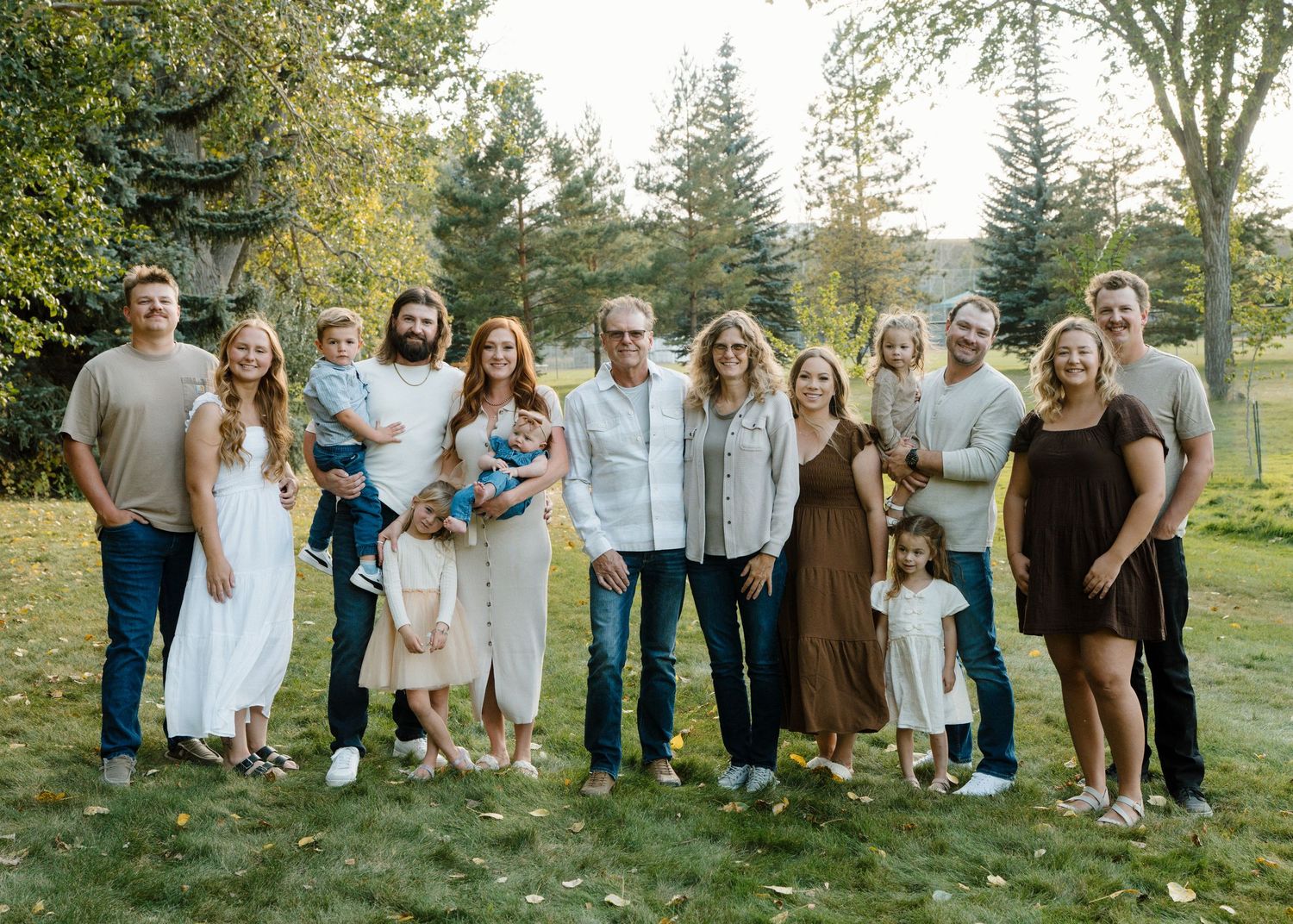 Large family group portrait smiling together outdoors on green lawn with trees behind.
