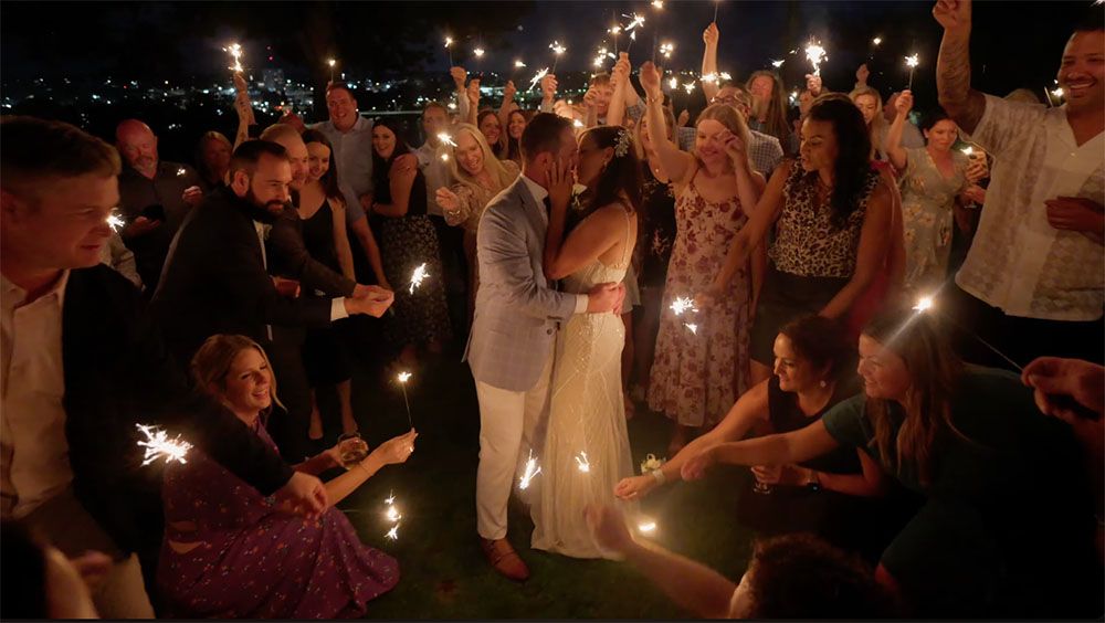 Bride and groom share first dance surrounded by wedding guests holding sparklers at night.