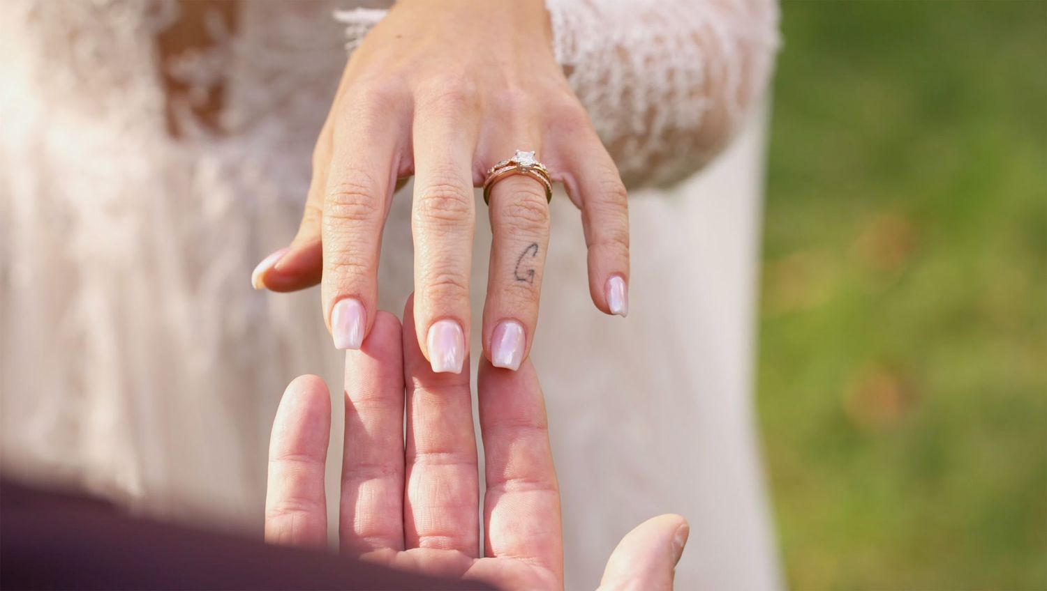 Close-up of a bride's hand wearing a gold engagement ring with pink manicured nails on wedding day.