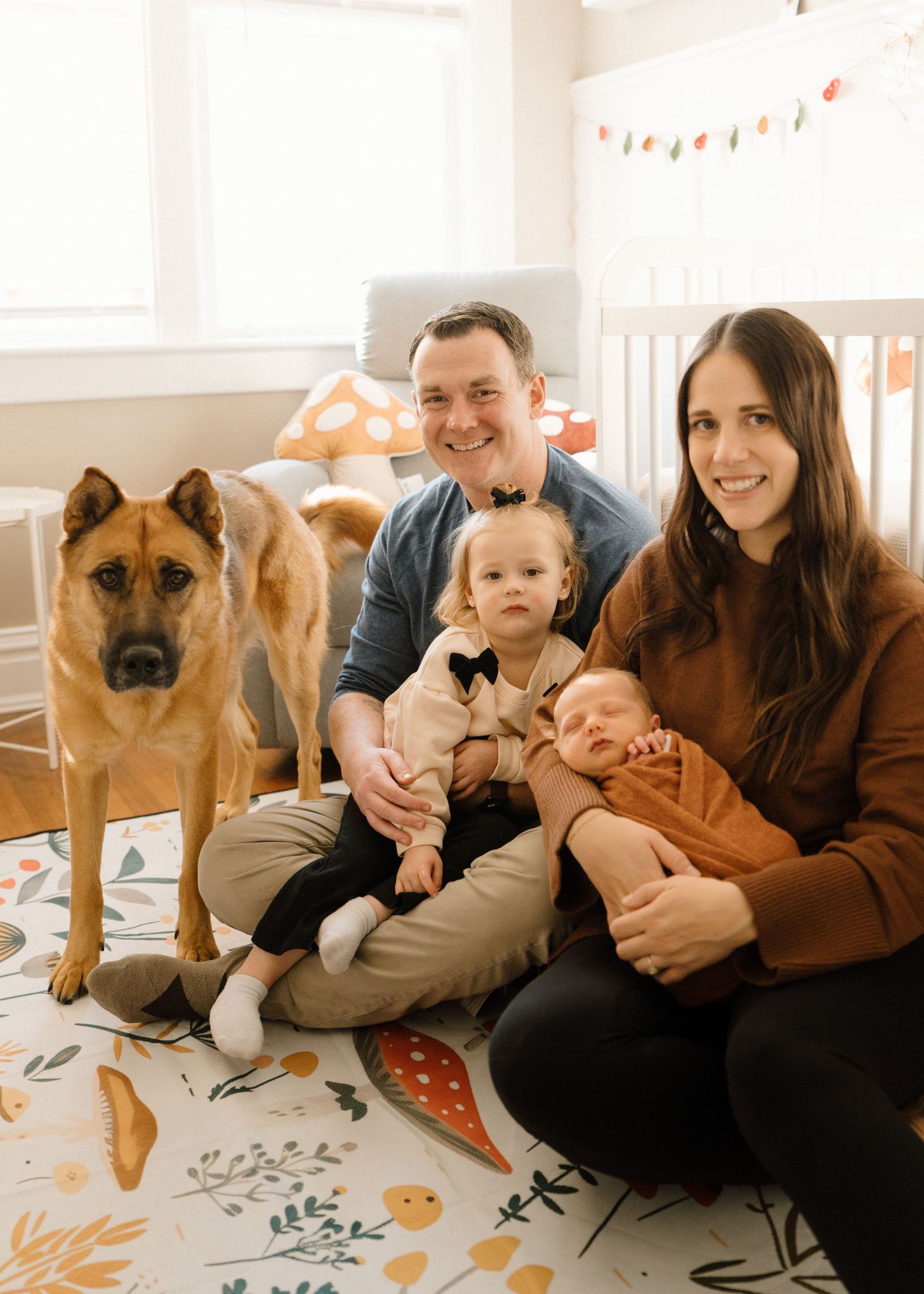 Happy family with two young children and a large dog posing together in a bright decorated nursery.