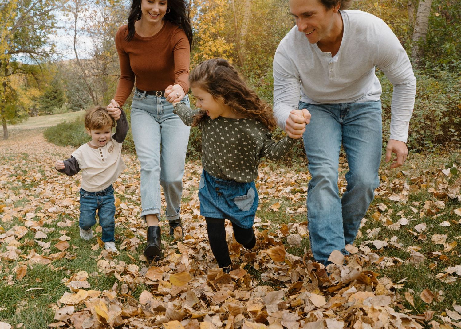 Happy family of four plays in autumn leaves together in a colorful fall park setting.