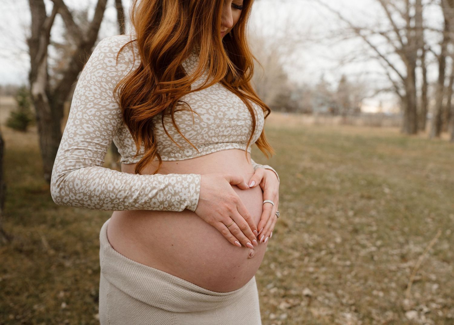 Pregnant woman cradles her baby bump with a heart shape outdoors in a maternity photo session.
