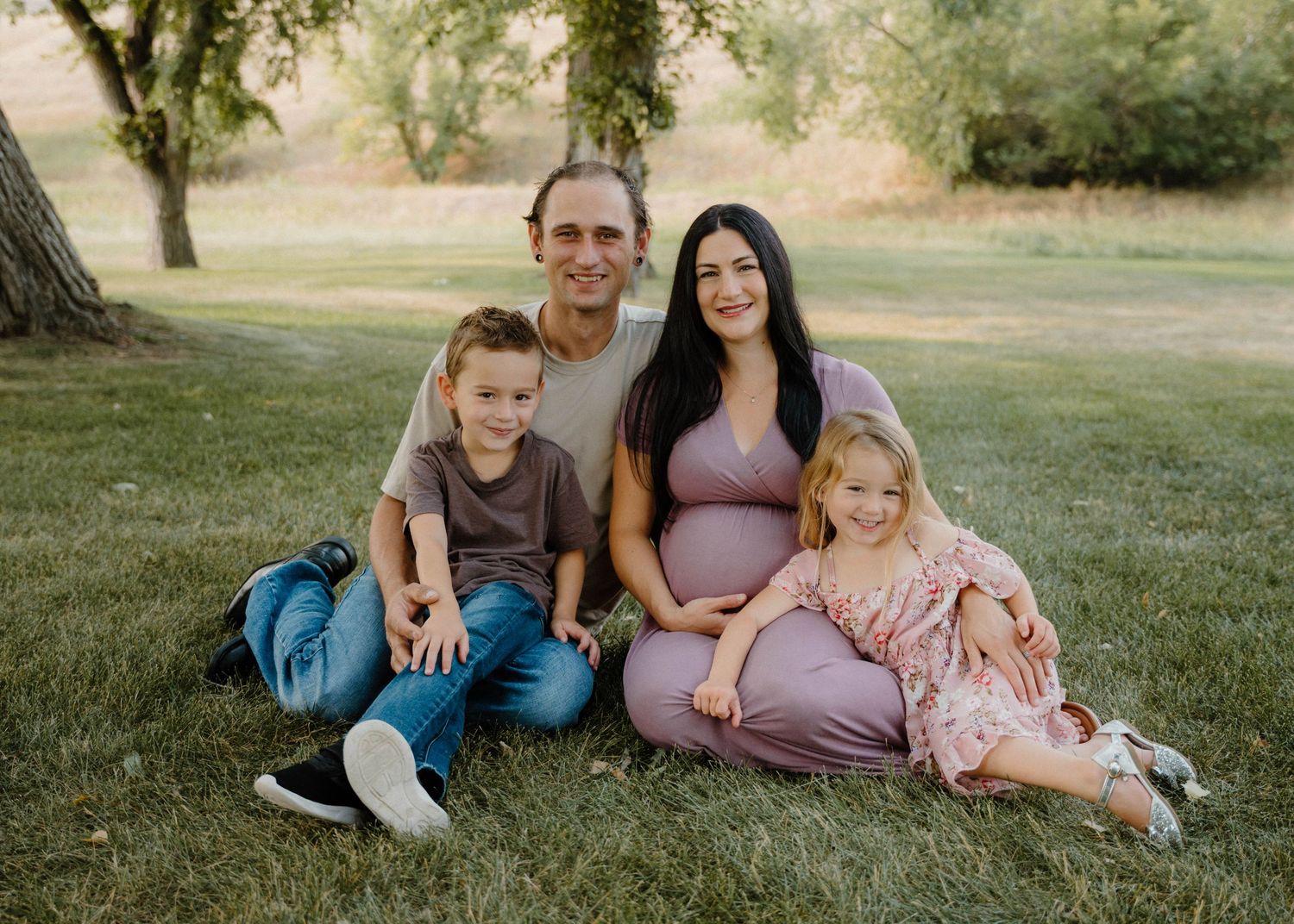 Family maternity photo session on grass with pregnant mother in mauve dress, father, son, and daughter smiling outdoors.