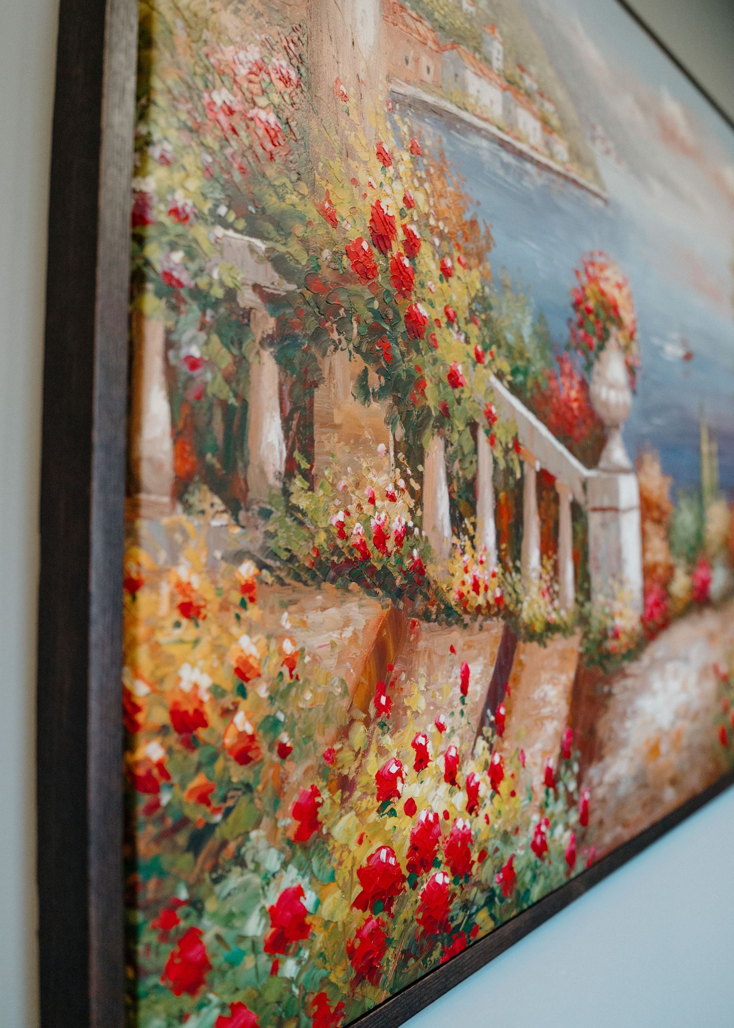 Framed oil painting of a lush garden with vibrant red roses climbing white columns near a Mediterranean villa.