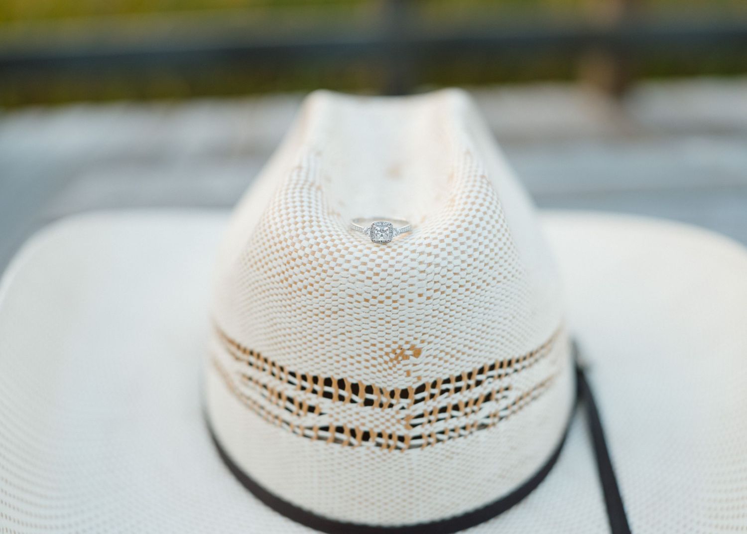 Close-up of white woven straw cowboy hat with dark band on wooden surface.