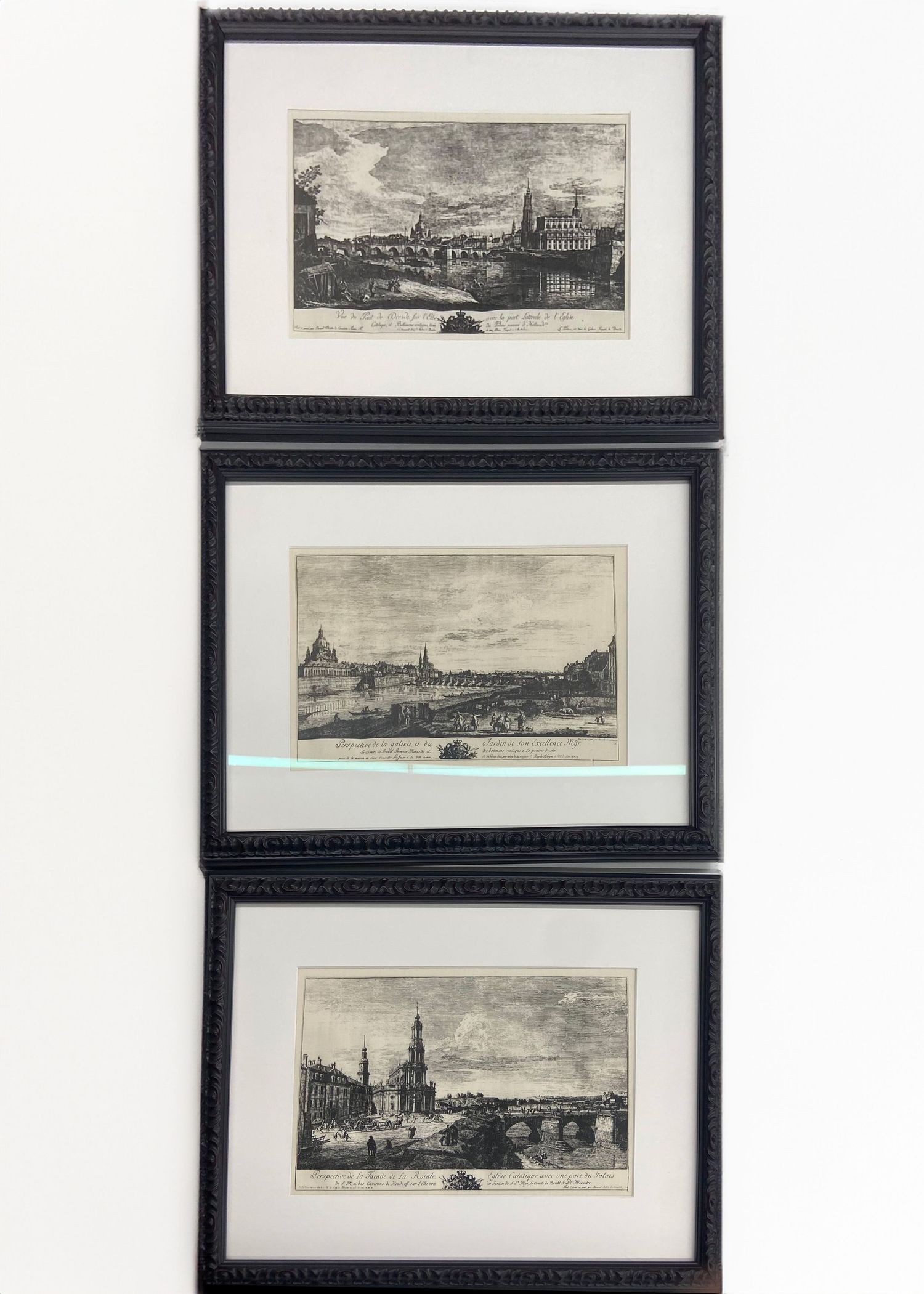 Set of three black framed antique city landscape engravings displayed on white wall.