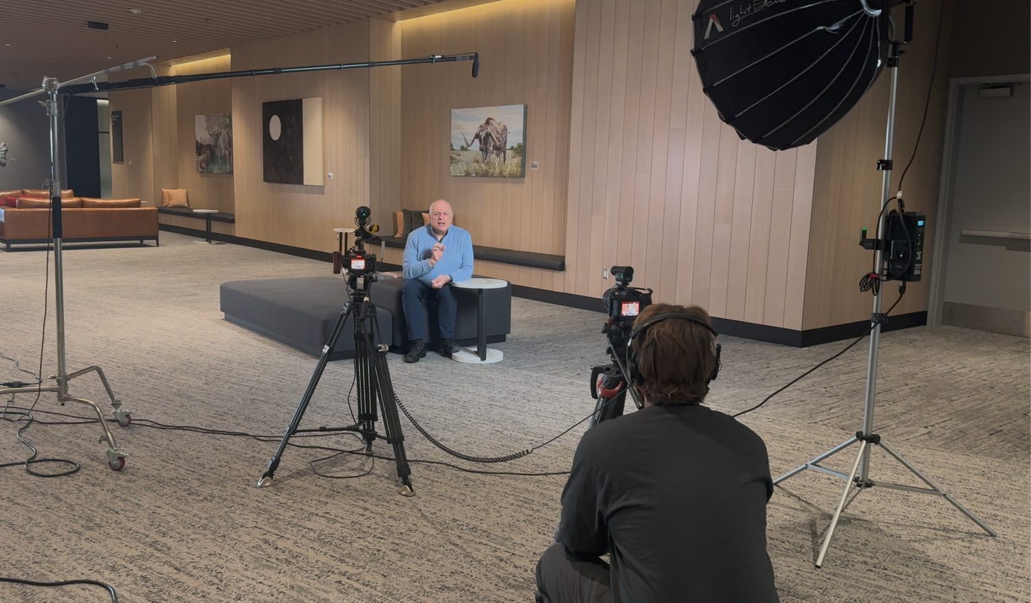 A man being filmed in an indoor studio setup with cameras, tripods, and a softbox light during a video production shoot.