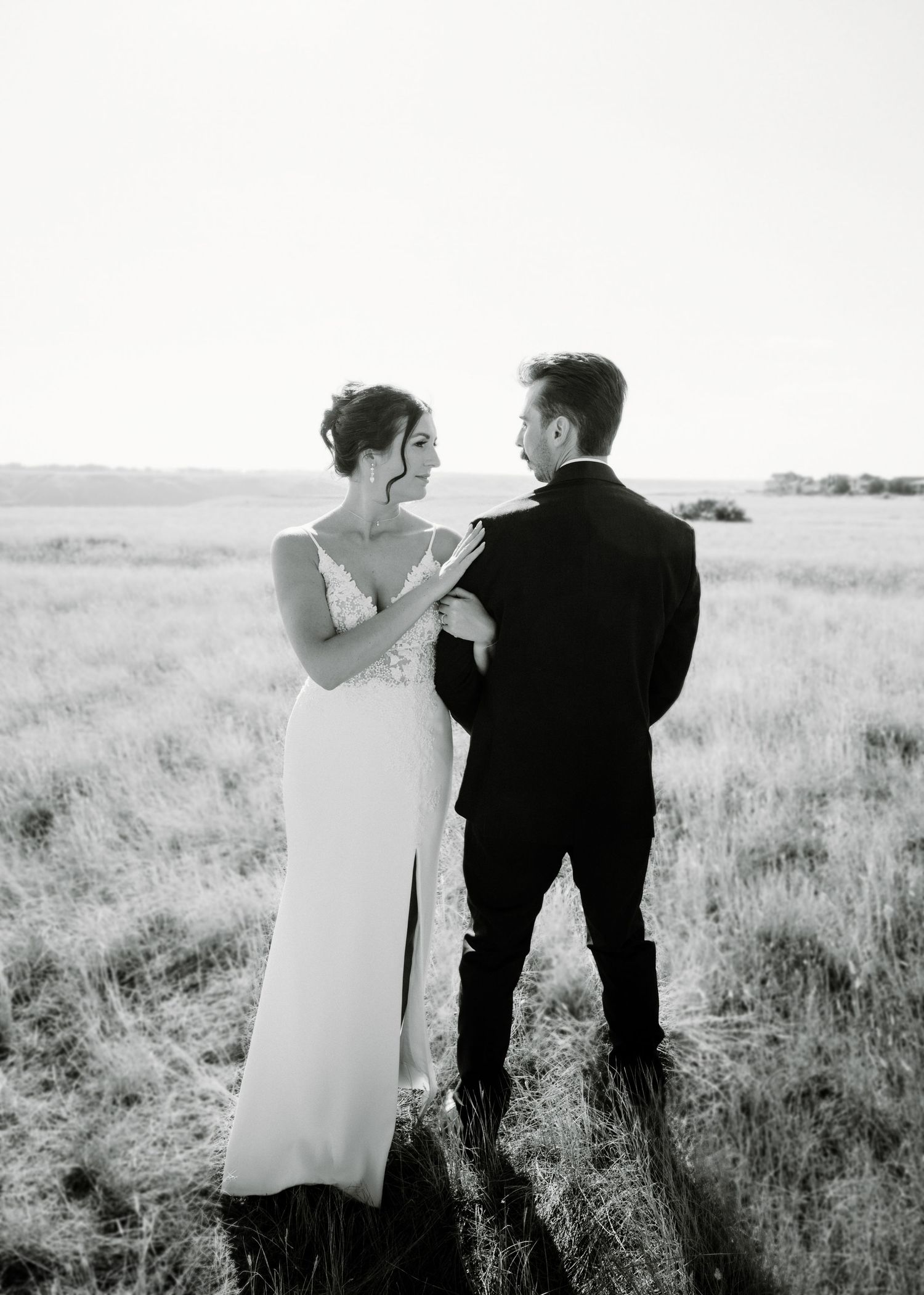 Bride and groom share a romantic moment in a vast open field at golden hour in black and white.
