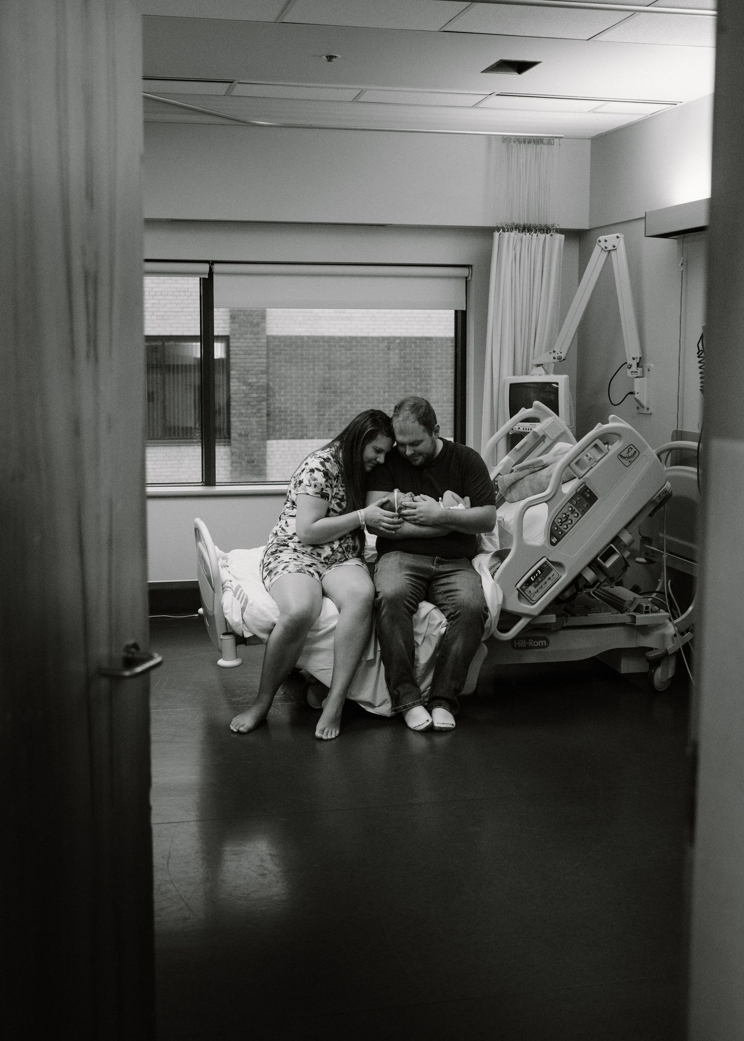 Black and white photo of new parents cradling newborn in a hospital room.