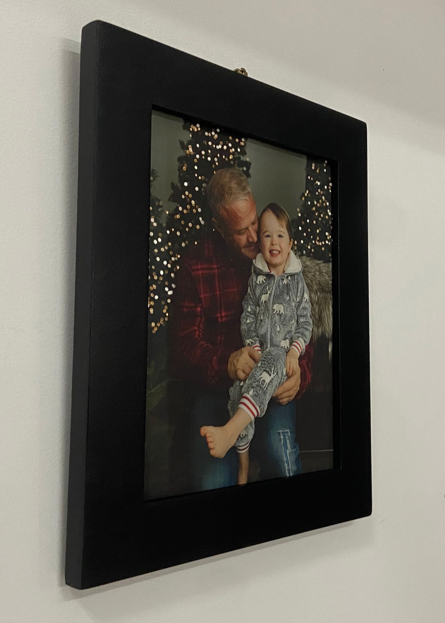 Black wood framed holiday portrait of grandfather and grandchild with Christmas lights.