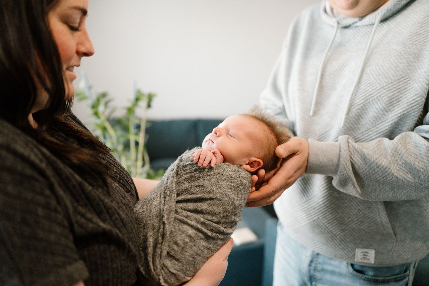 New parents in casual clothing lovingly cradle their swaddled sleeping newborn baby together.