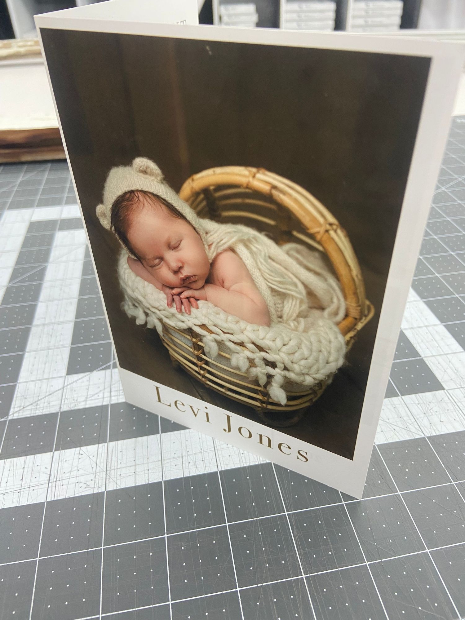 Newborn baby sleeping in wicker basket with knit bear hat on birth announcement card.