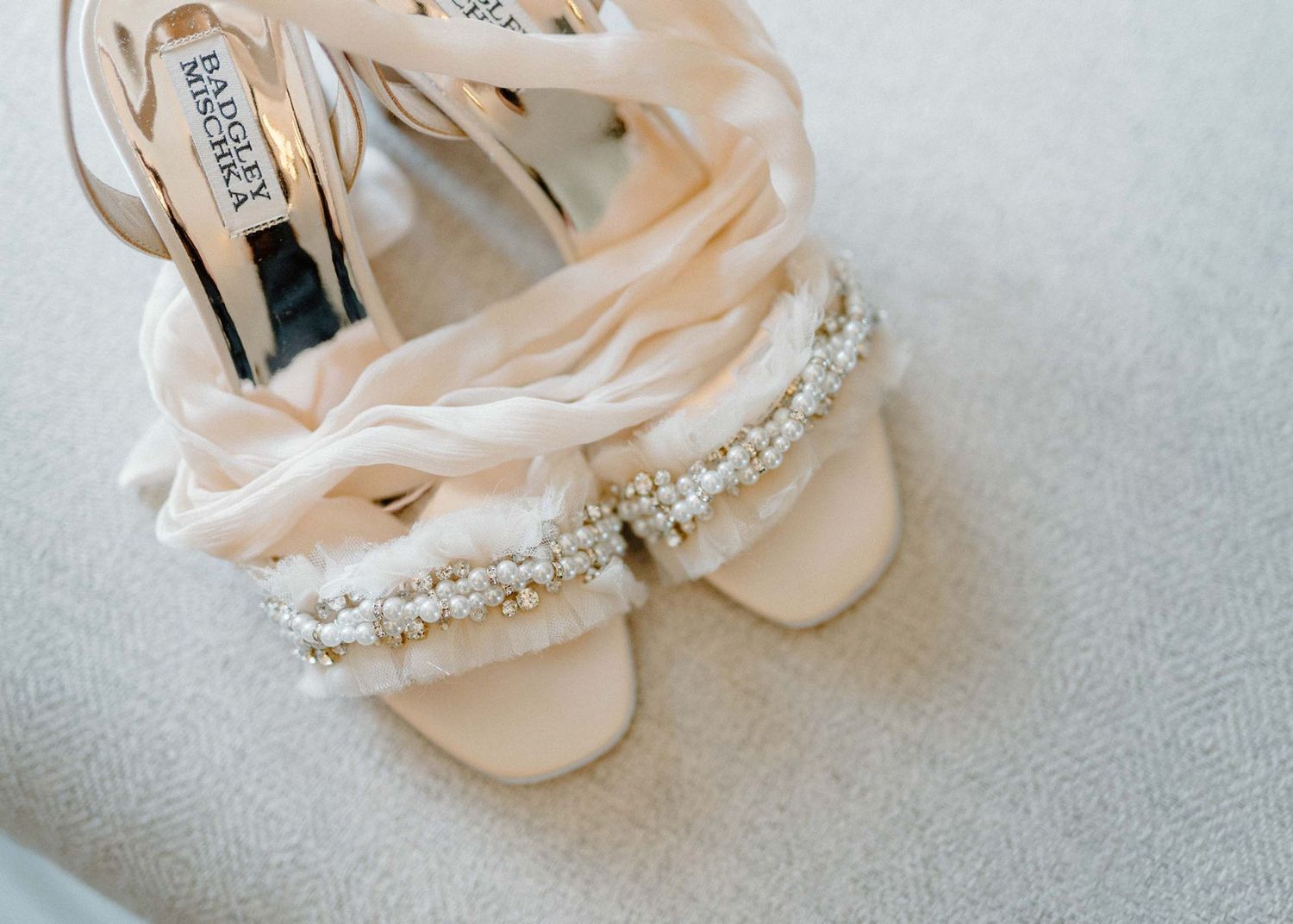 Badgley Mischka bridal heels with pearl embellishments and blush chiffon straps on a soft gray surface.
