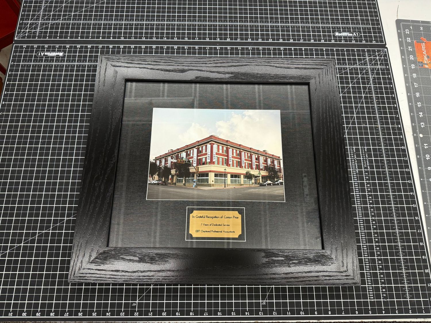 Vintage building photo in black wood frame with gold engraved plaque on cutting mat.