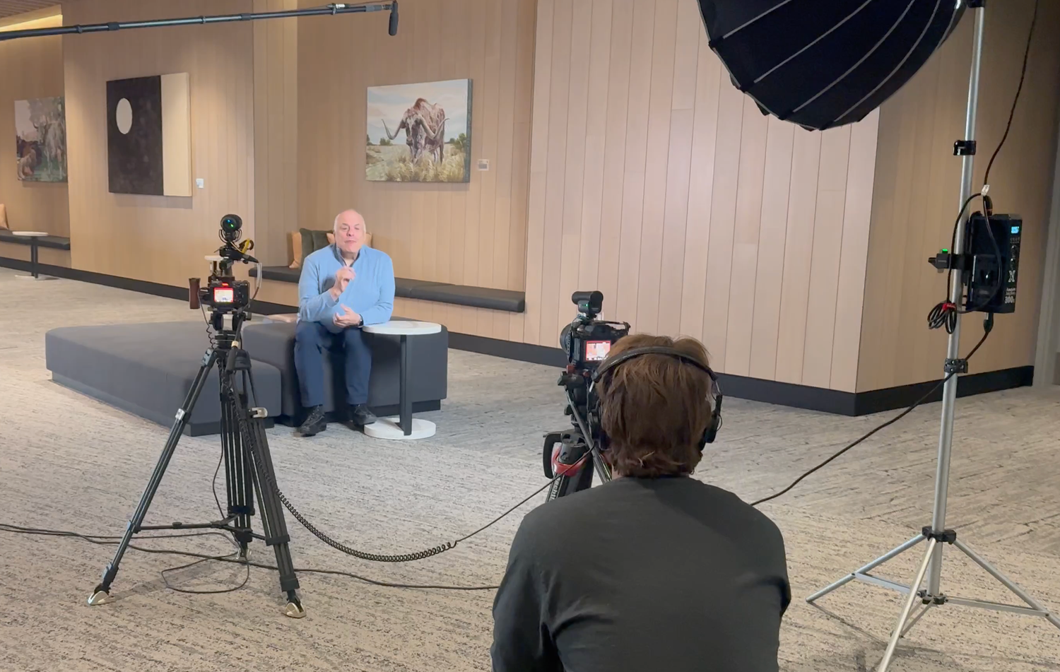 Professional video production crew filming a man being interviewed under studio lighting in a modern building lobby.
