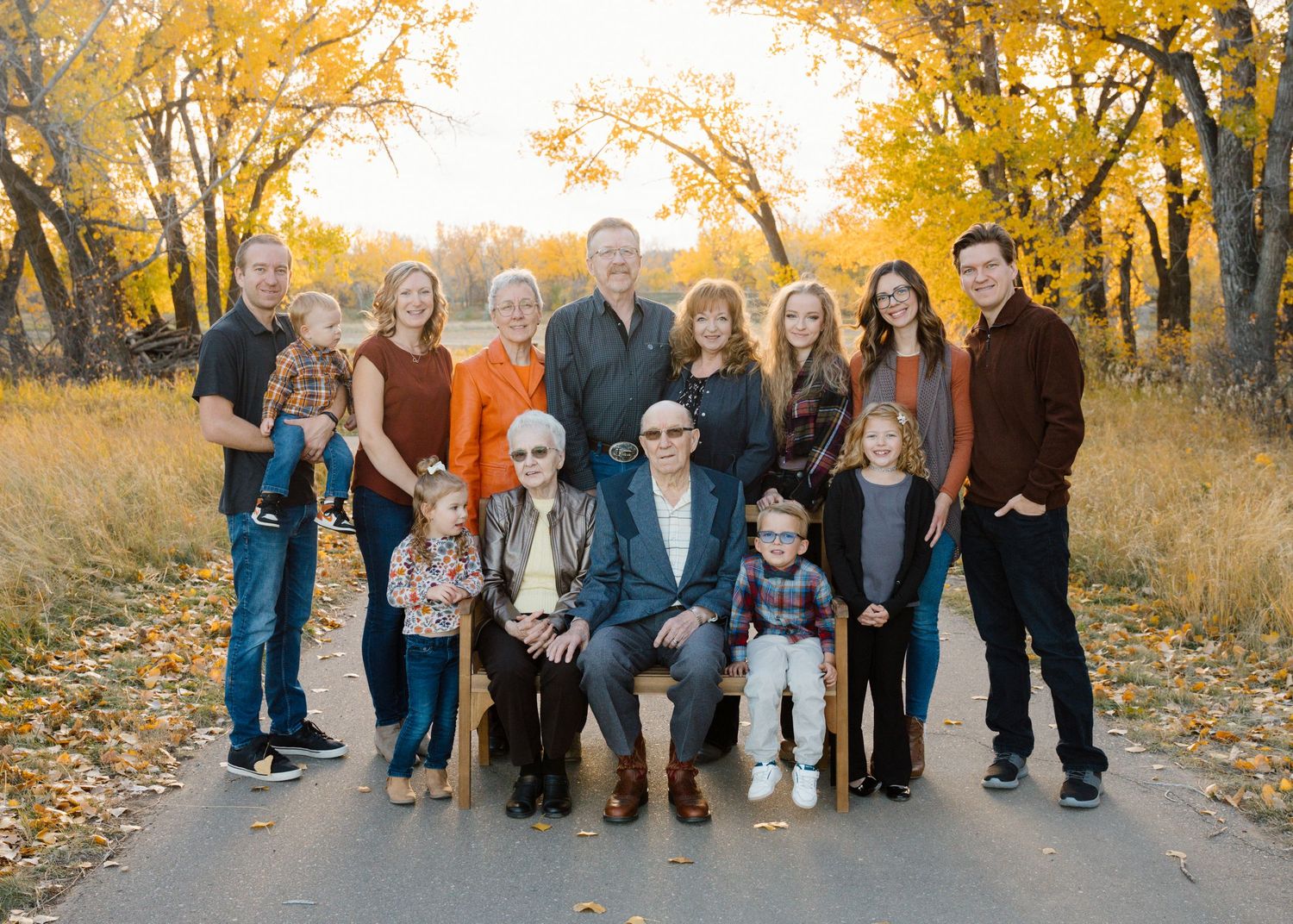 Large multigenerational family portrait outdoors in autumn with golden foliage background.