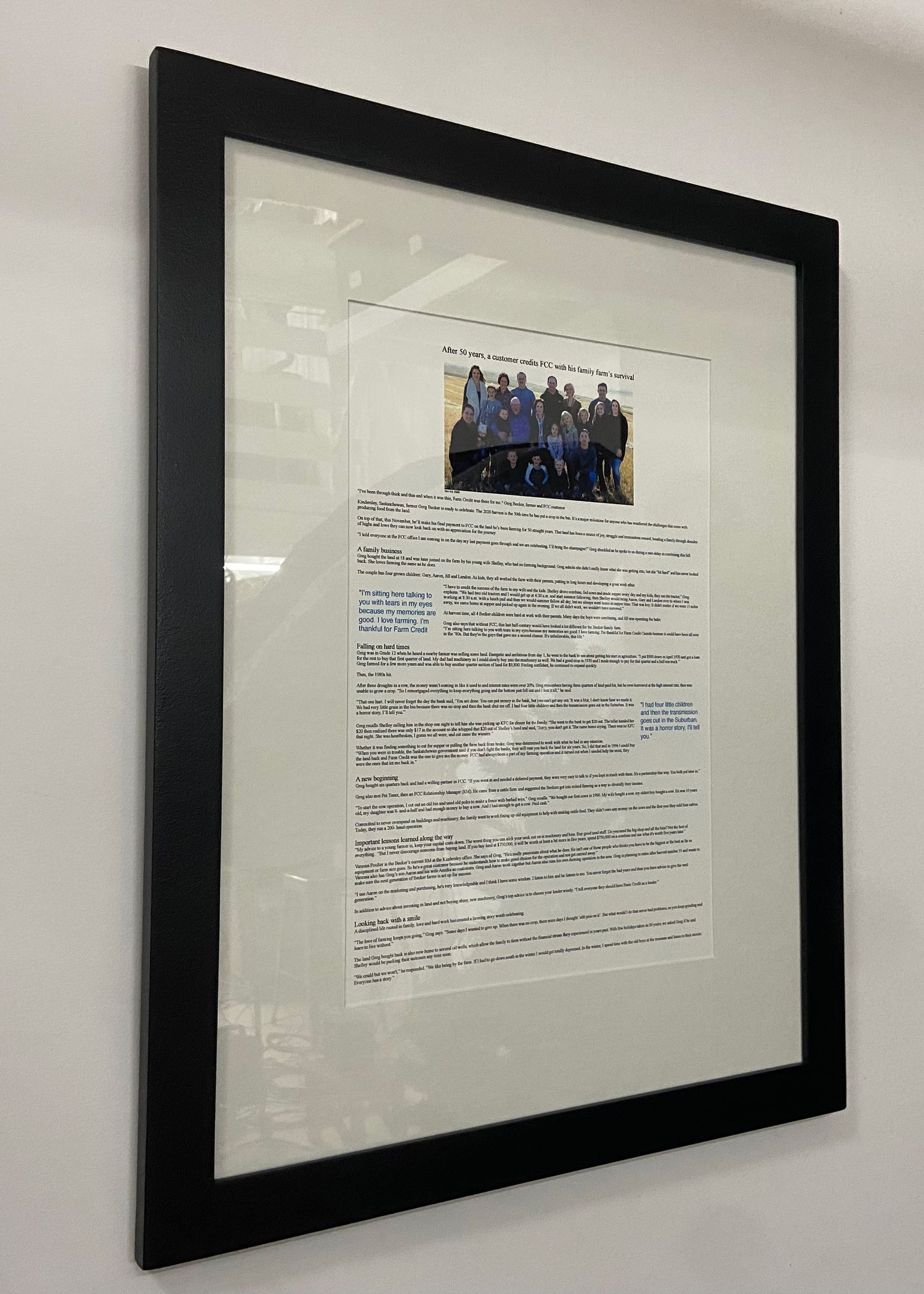 Black framed document with group photo and text mounted on white wall in office setting.